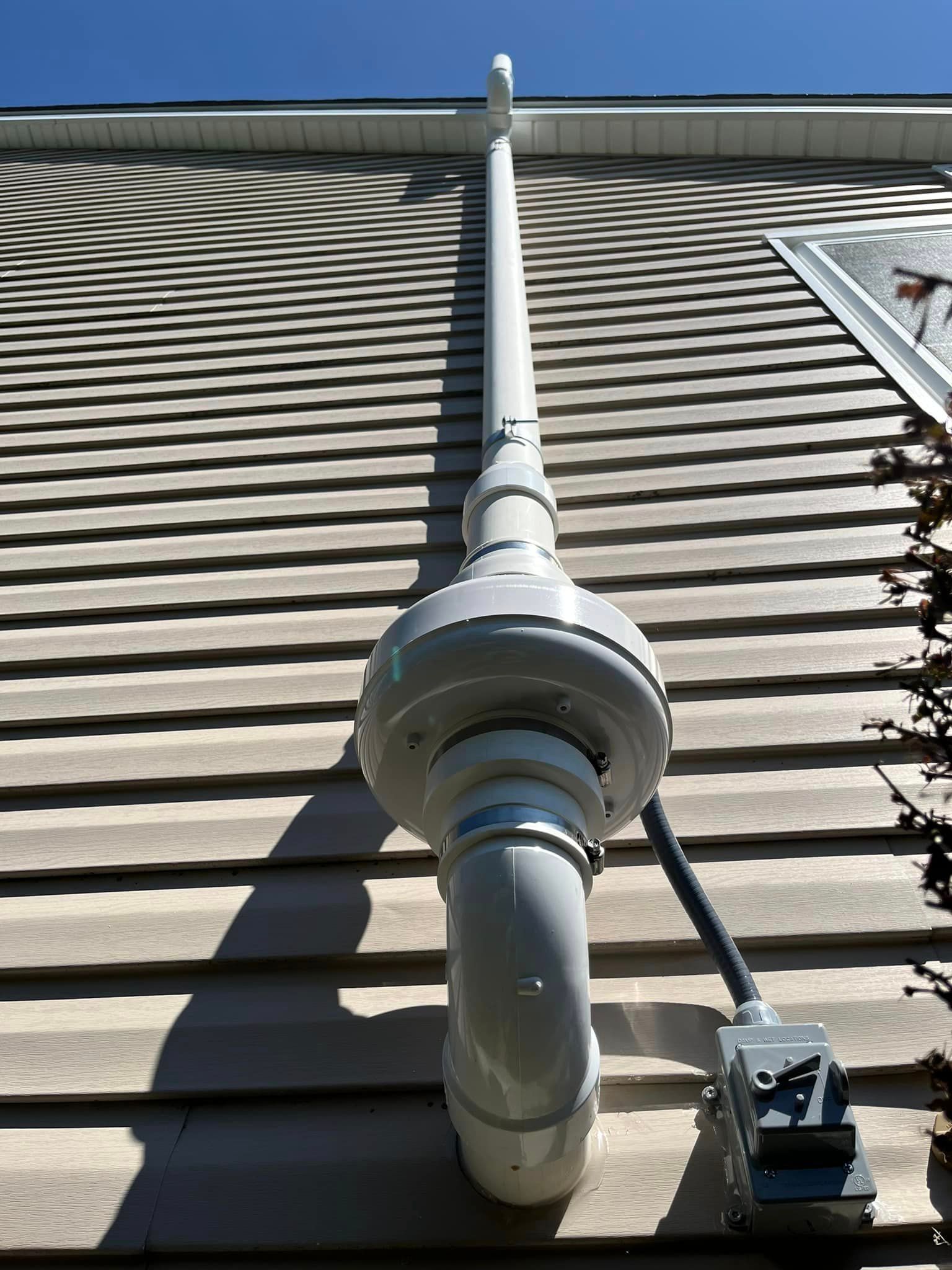 A white pipe is attached to the side of a house