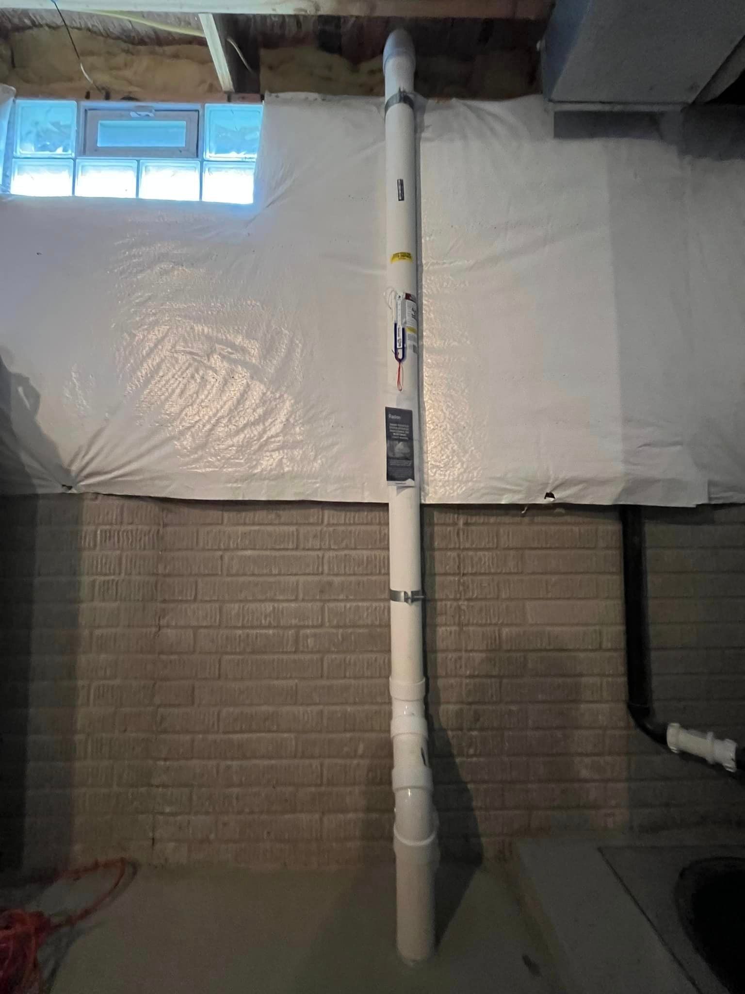 A white pipe is sitting in a basement next to a brick wall.