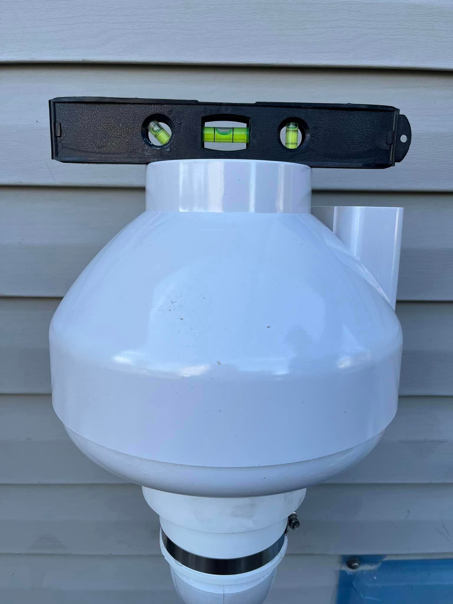 A white pipe with a level attached to it is hanging on a wall.