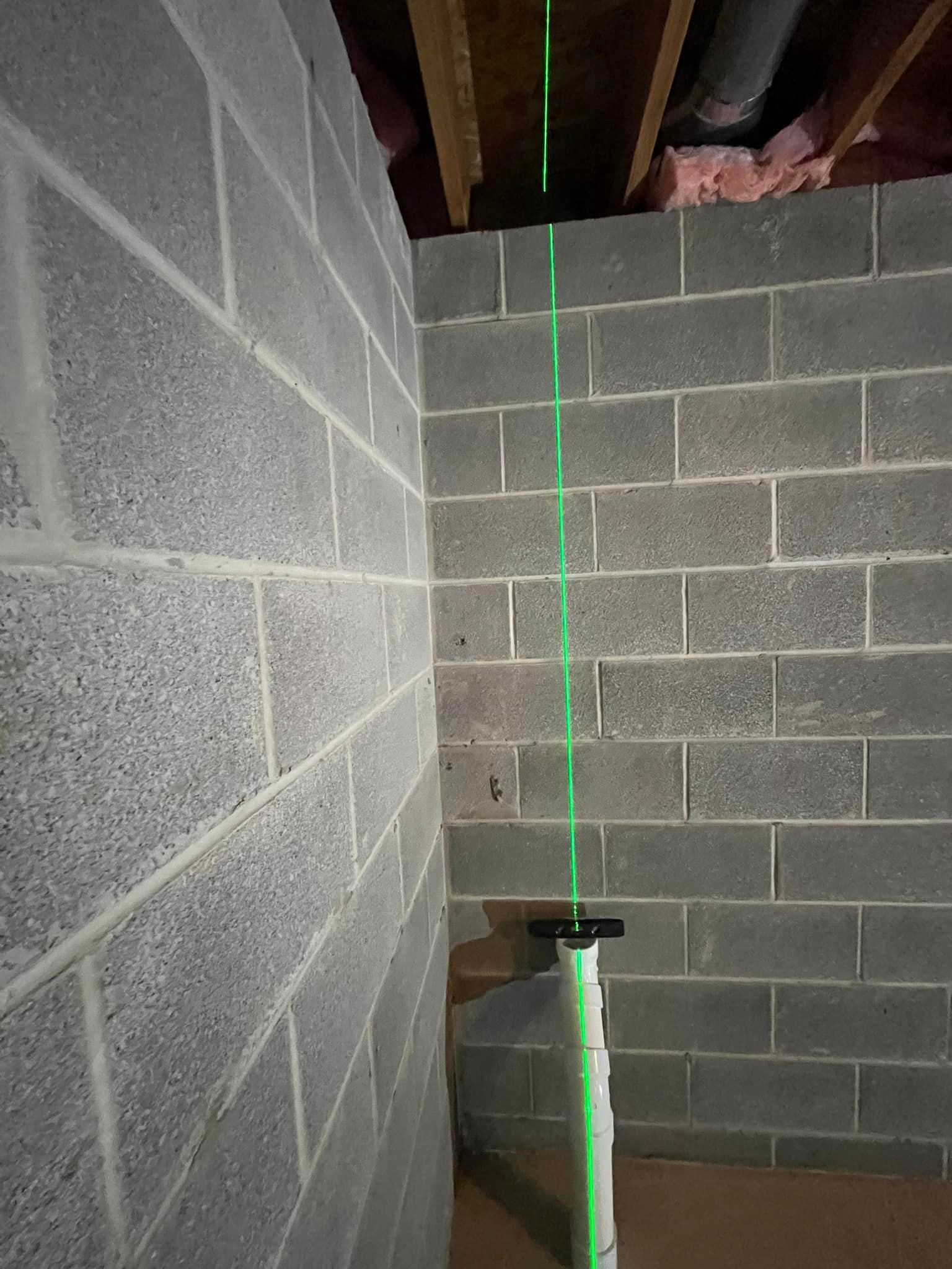A green laser is being used to measure a brick wall in a basement.