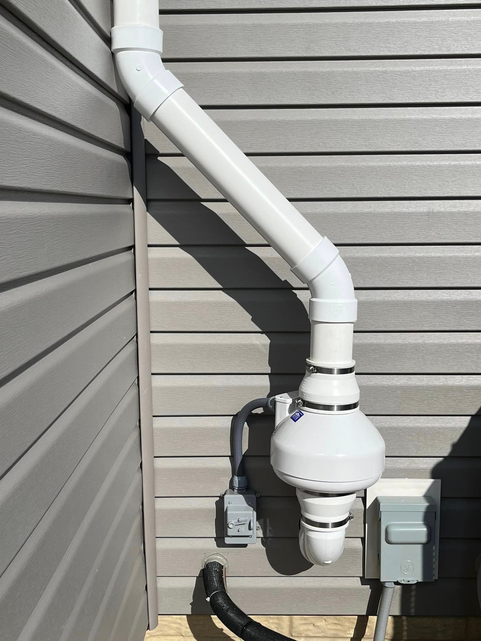 A white pipe is attached to the side of a house.