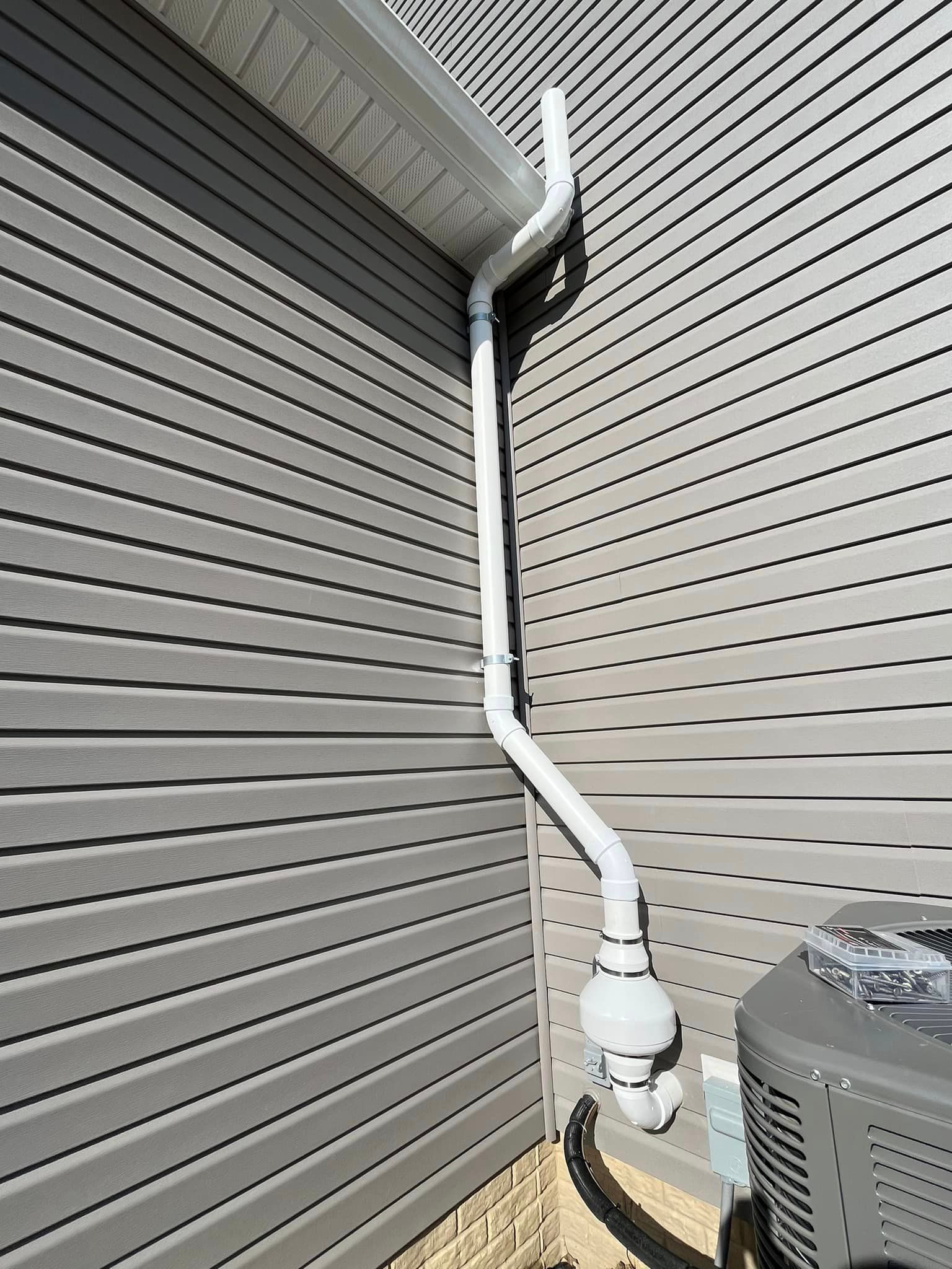 A white pipe is attached to the side of a house next to an air conditioner.