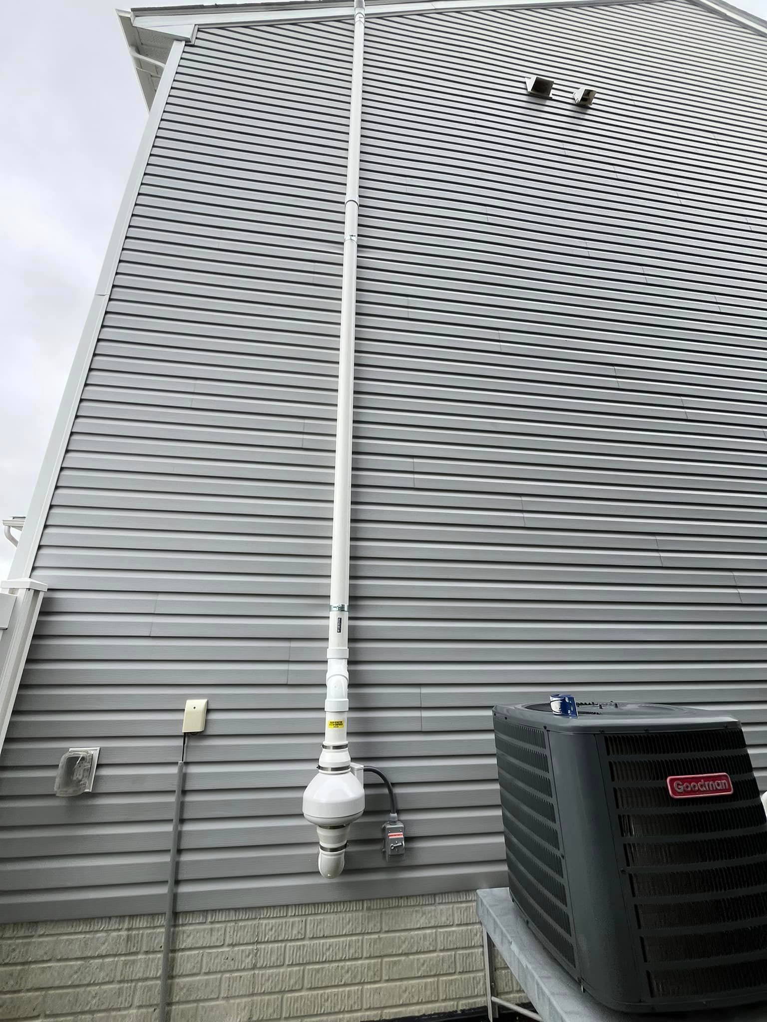 A house with a gray siding and a black air conditioner on the side of it.