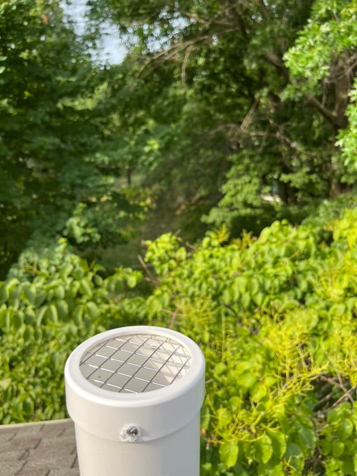 A white pipe is sitting on top of a roof next to trees.