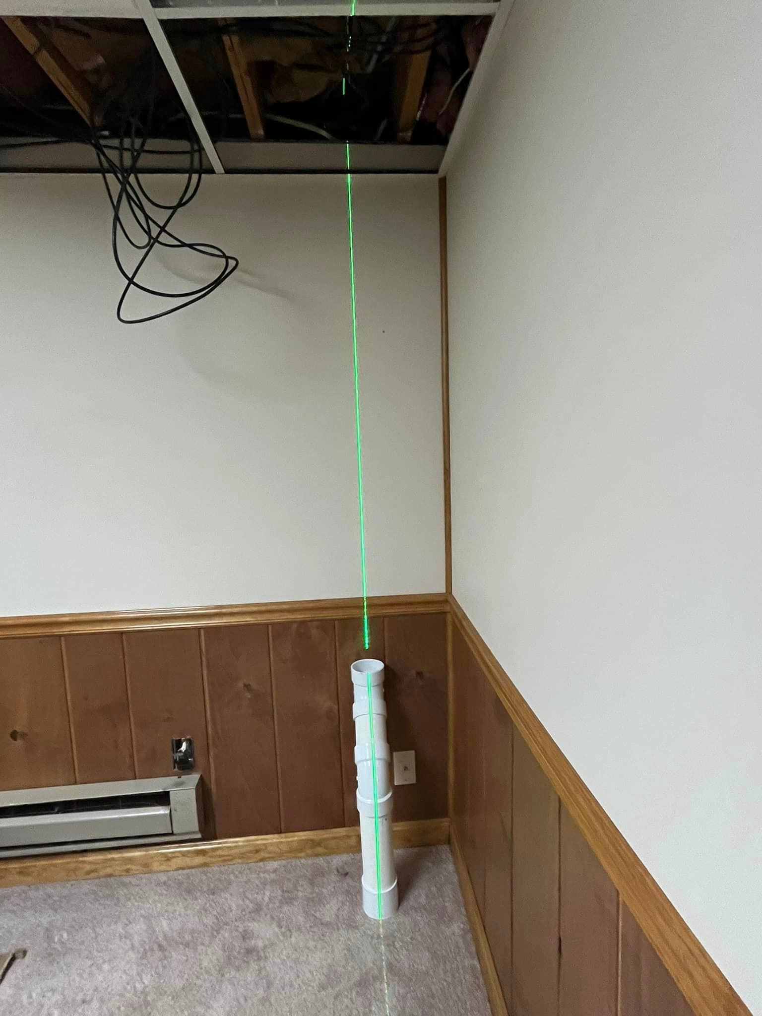 A green laser is being used to measure a pipe in a room.