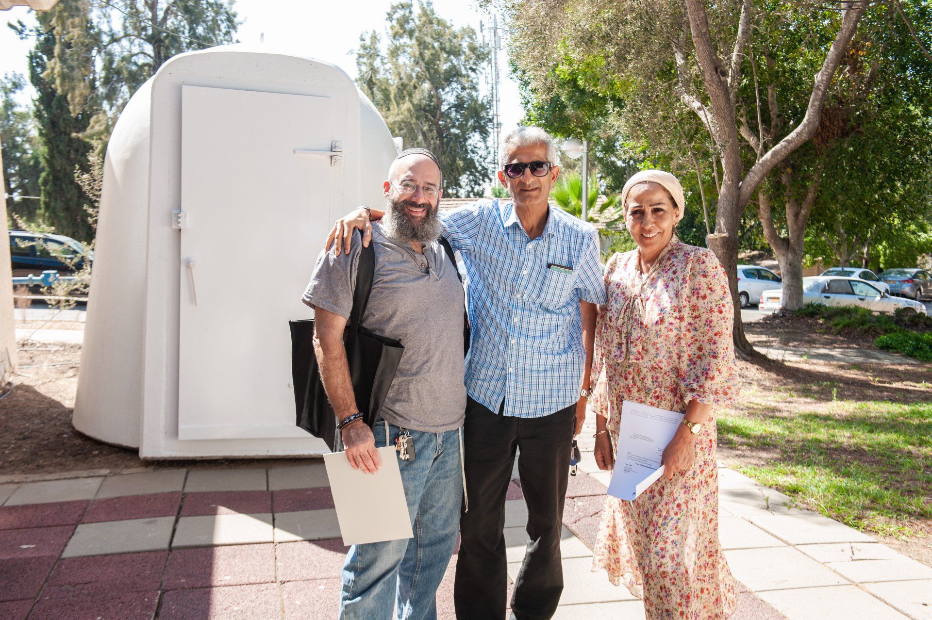Three people are posing for a picture in front of a white Shelter