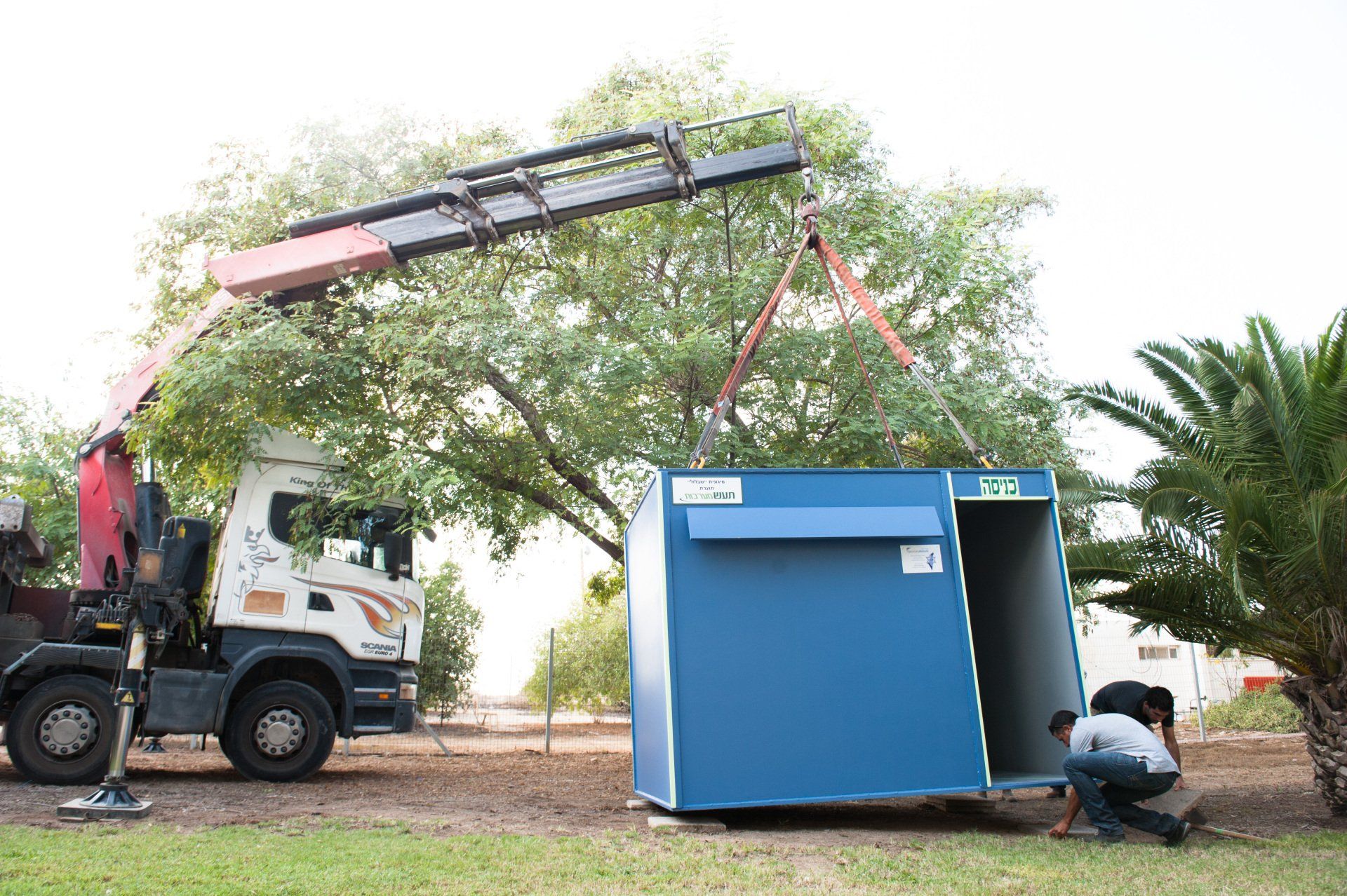 A crane is lifting a blue Shelter into the air.