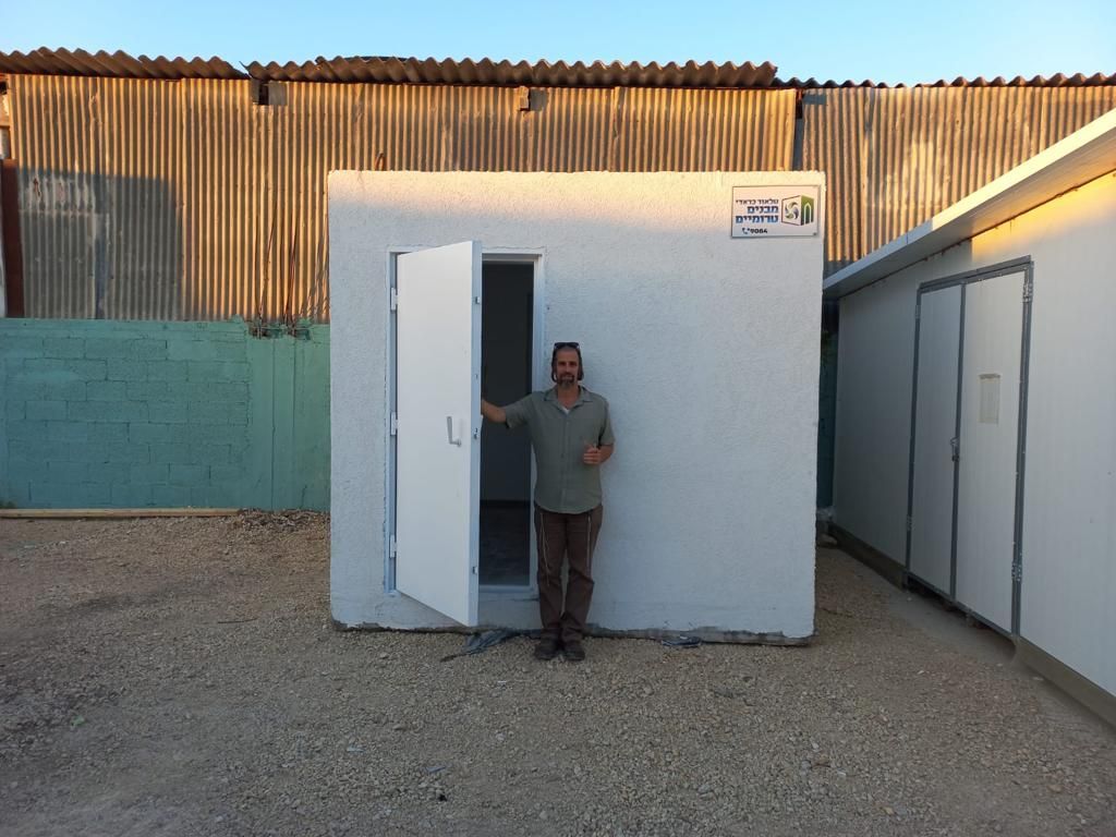A man is standing in front of a small white building