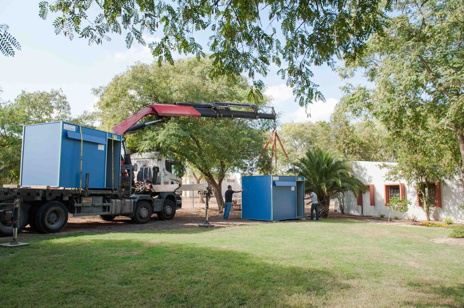 A truck with a crane attached to it is carrying blue shelter