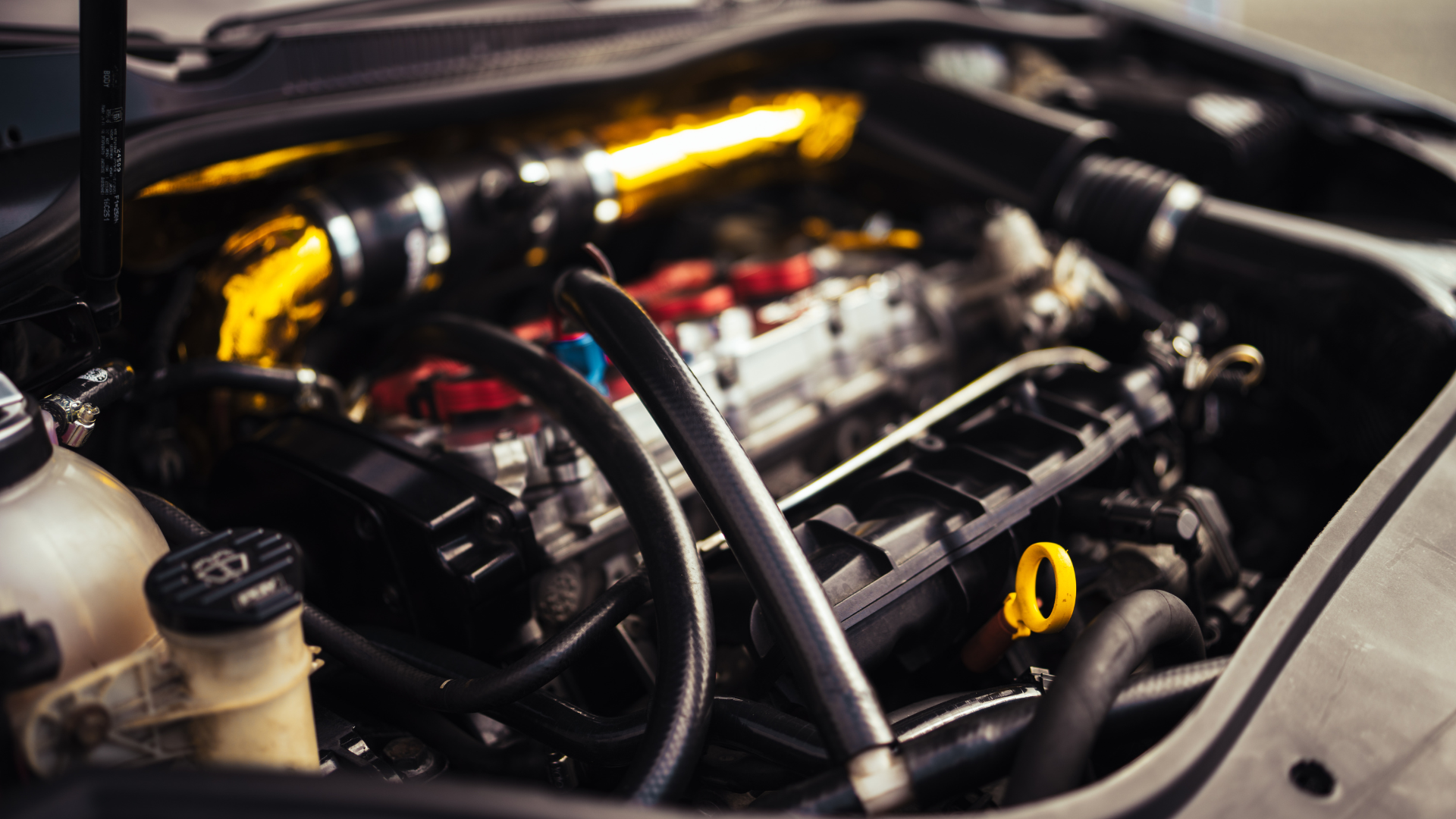 Car engine bay with gold intake, black tubes, and yellow dipstick.