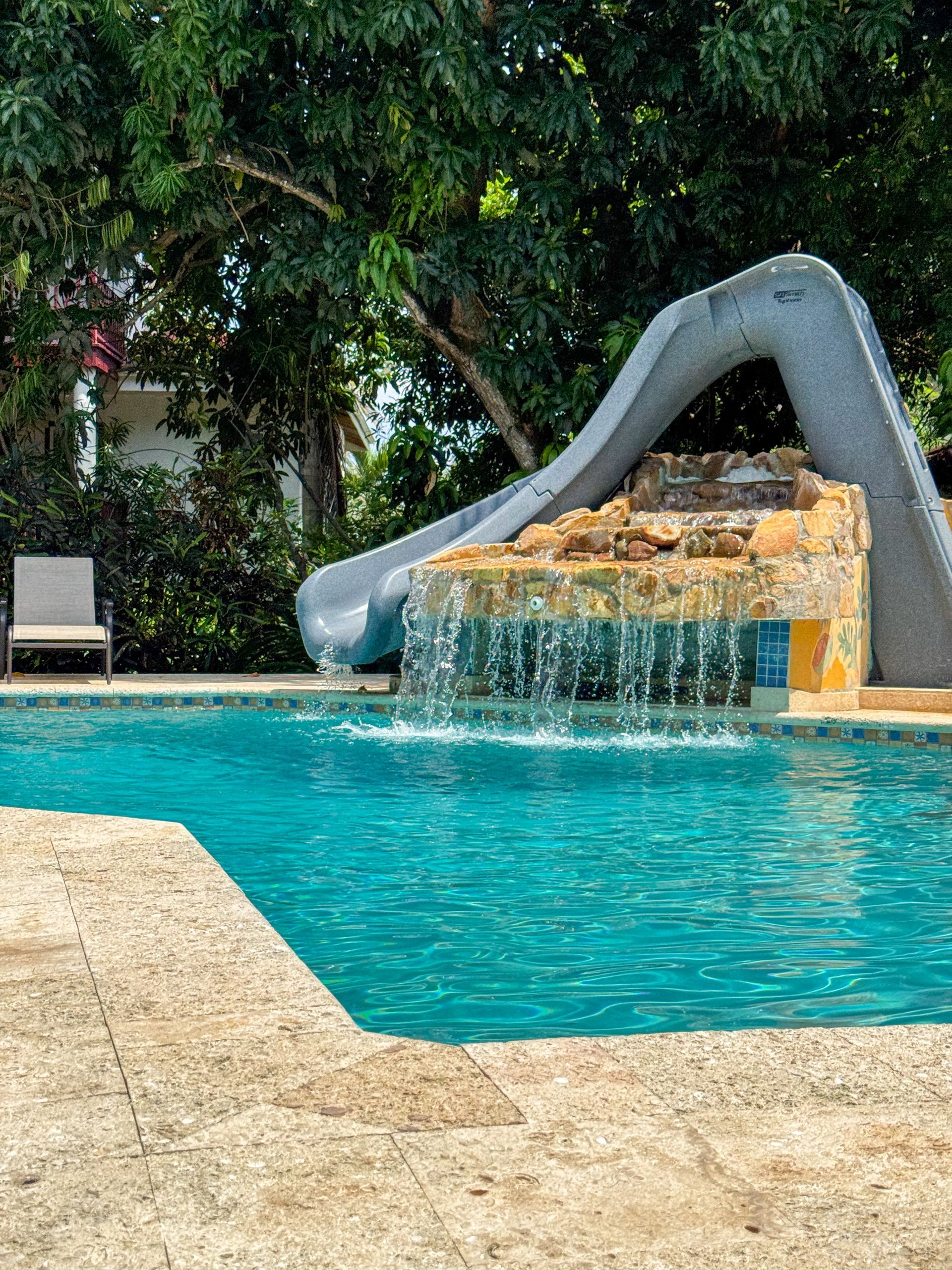 A large swimming pool with a water slide and a waterfall.