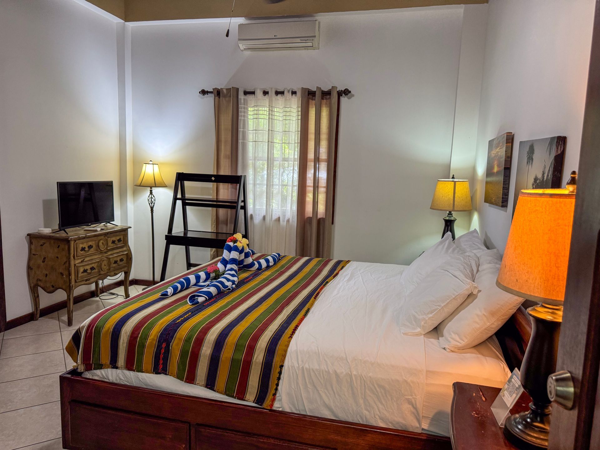 A bedroom with a large bed , two lamps , a desk and a television.