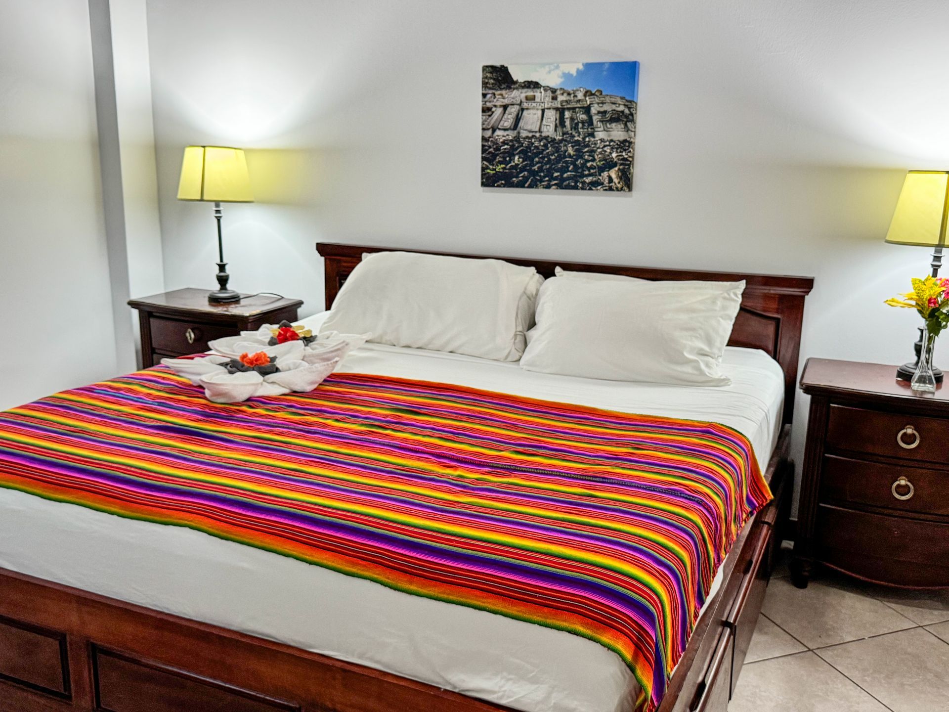 A bedroom with a bed , nightstand , lamps and a picture on the wall above the bed.