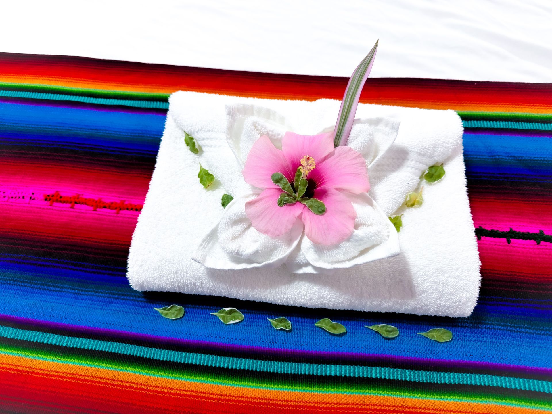 A white towel with a pink flower on top of it on a colorful blanket, Caribbean Shores B&B room, Hopkins Belize