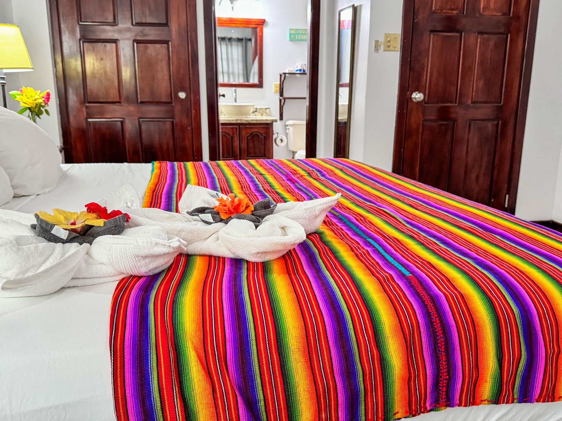 A bed with a colorful blanket and towels on it in a hotel room, affordable accommodations in Hopkins Village Belize