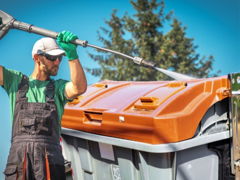 man pressure washing cleaning a dumpster