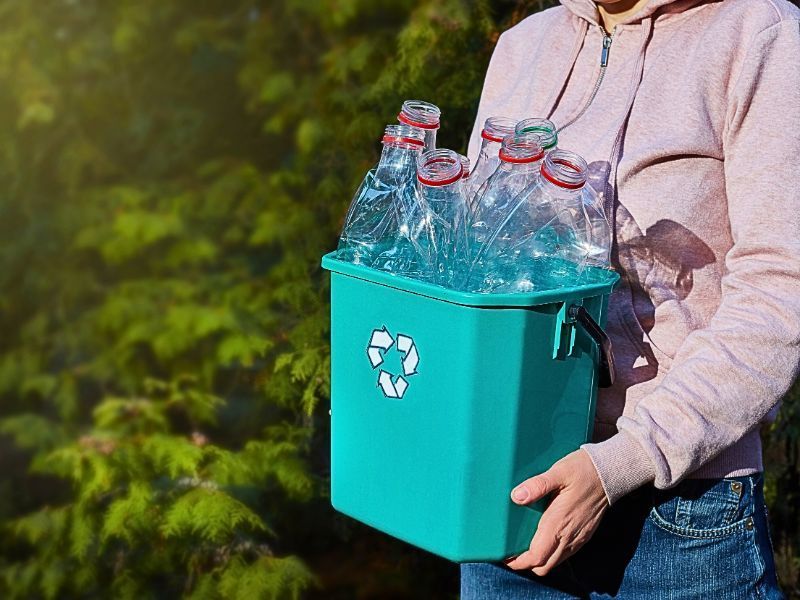 person holding container with plastic bottles for recycling