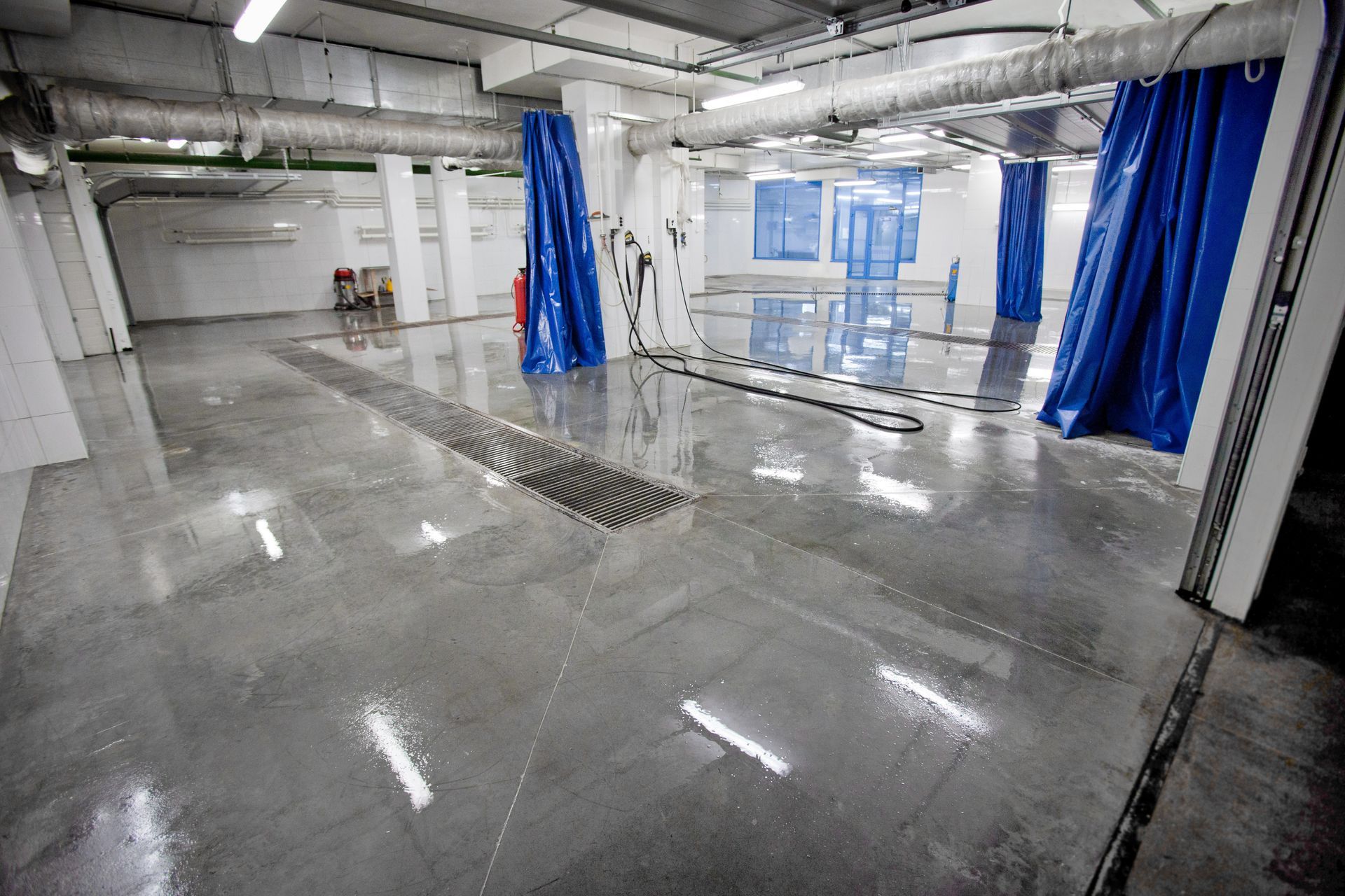 Pièce industrielle vide avec sol en béton humide, rideaux bleus et tuyaux au plafond