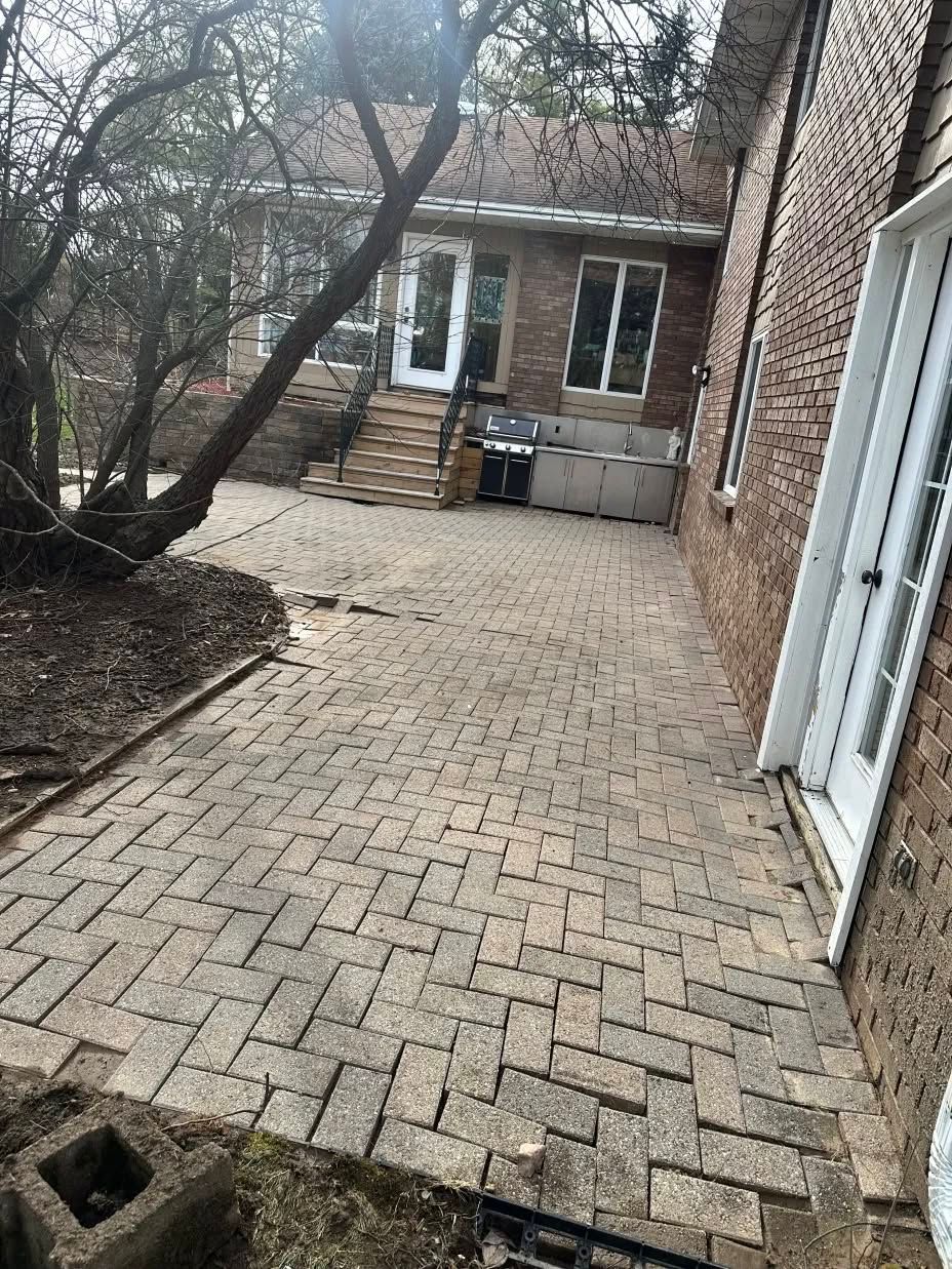 A brick patio in front of a brick house with a tree in the background.