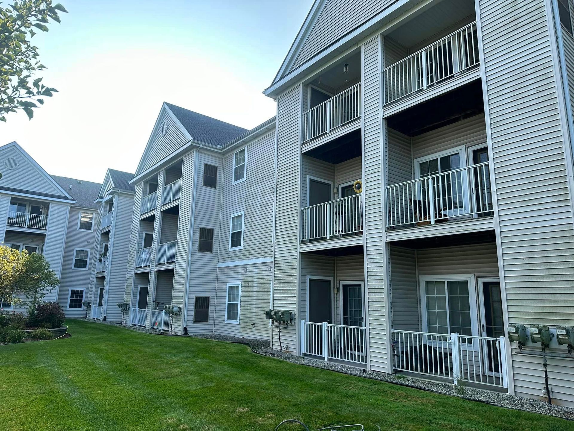 A large white apartment building with balconies and a lush green lawn in front of it.