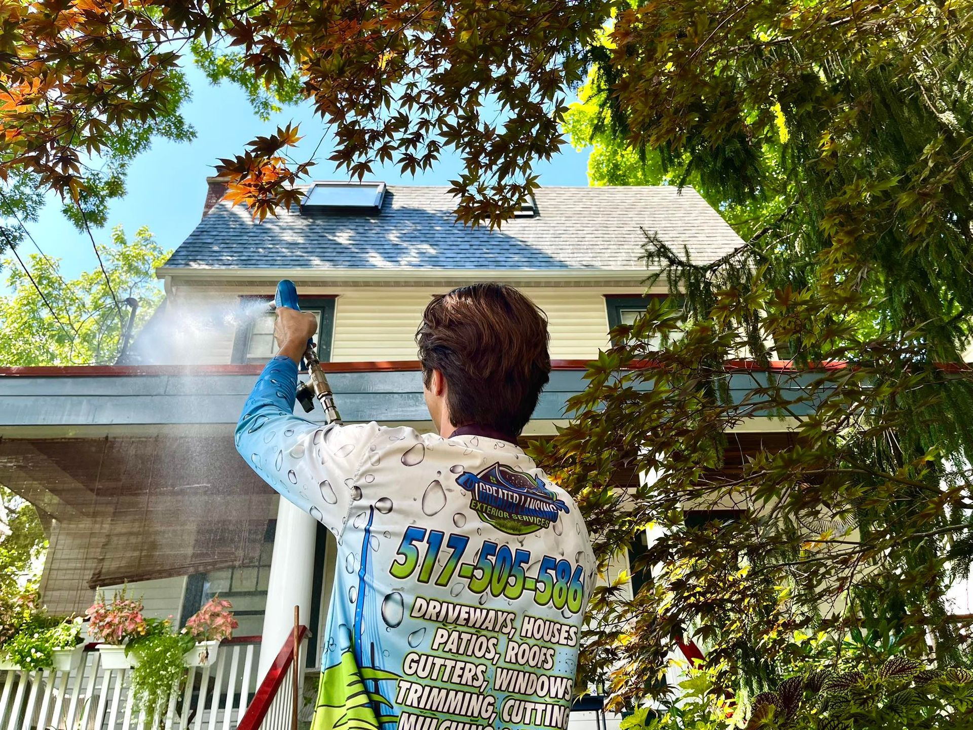 A man is cleaning the roof of a house with a pressure washer.