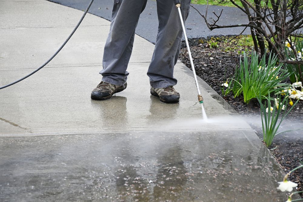 A person is using a high pressure washer to clean a sidewalk.