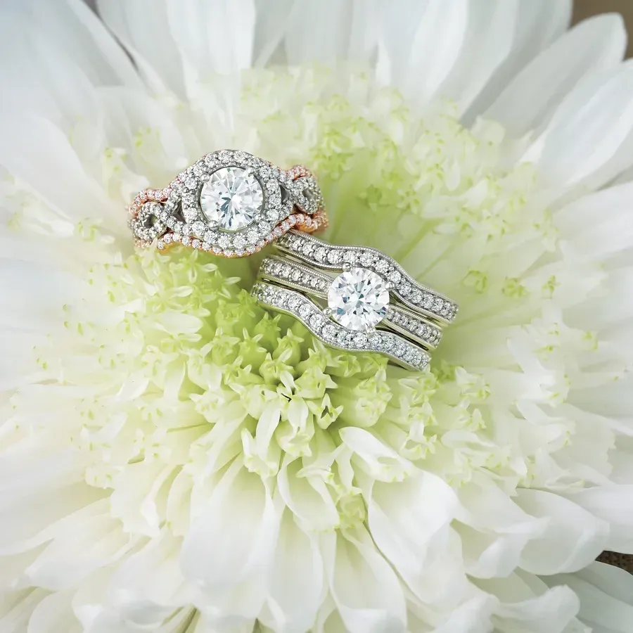 Two diamond rings displayed on white flower. One has rose gold detail.