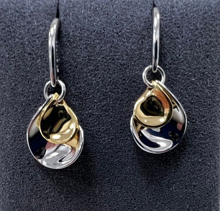 Two silver and gold teardrop earrings hanging against a dark background.