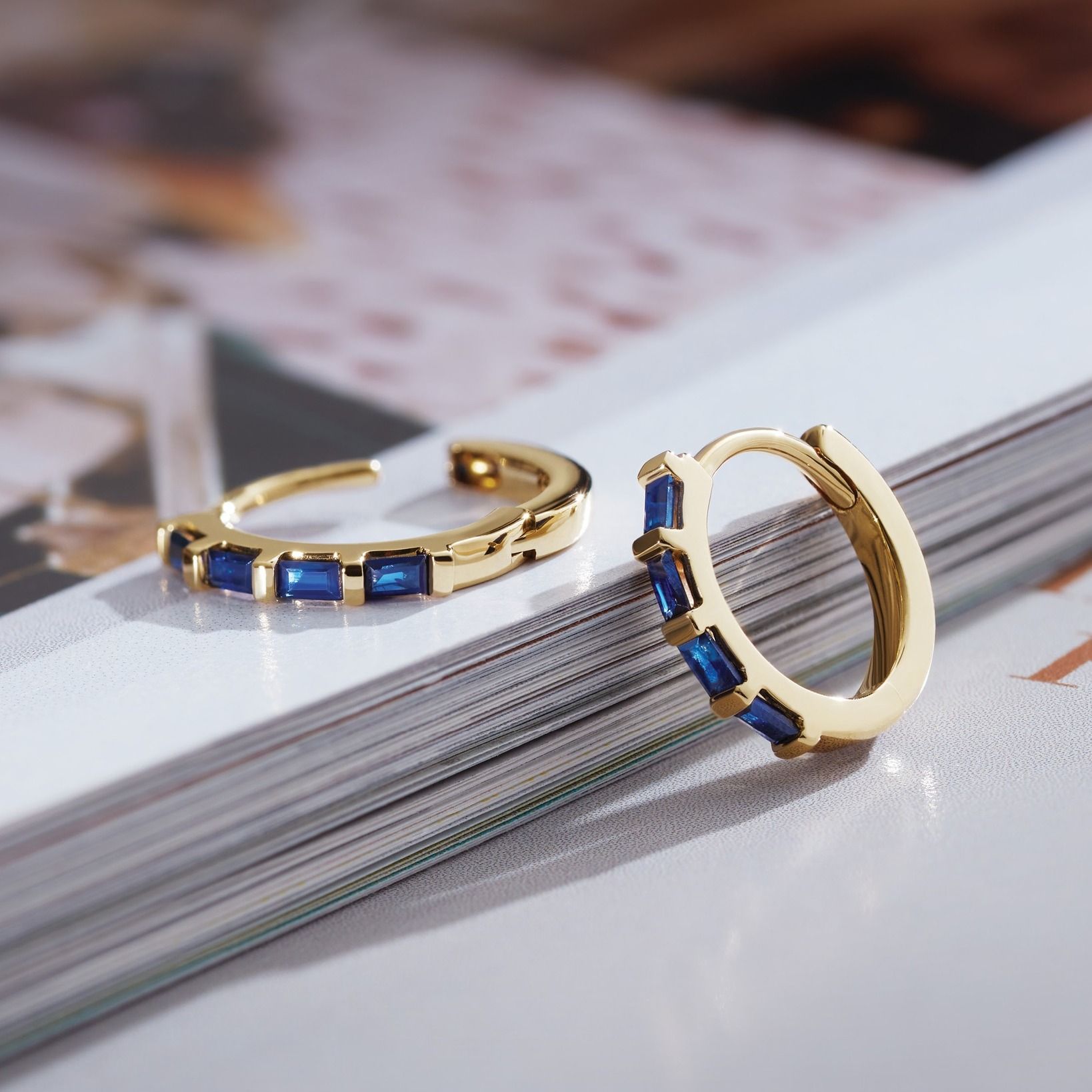 Gold hoop earrings with blue rectangular stones on a white background.