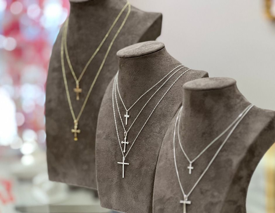 Necklaces with crosses displayed on gray mannequin busts.