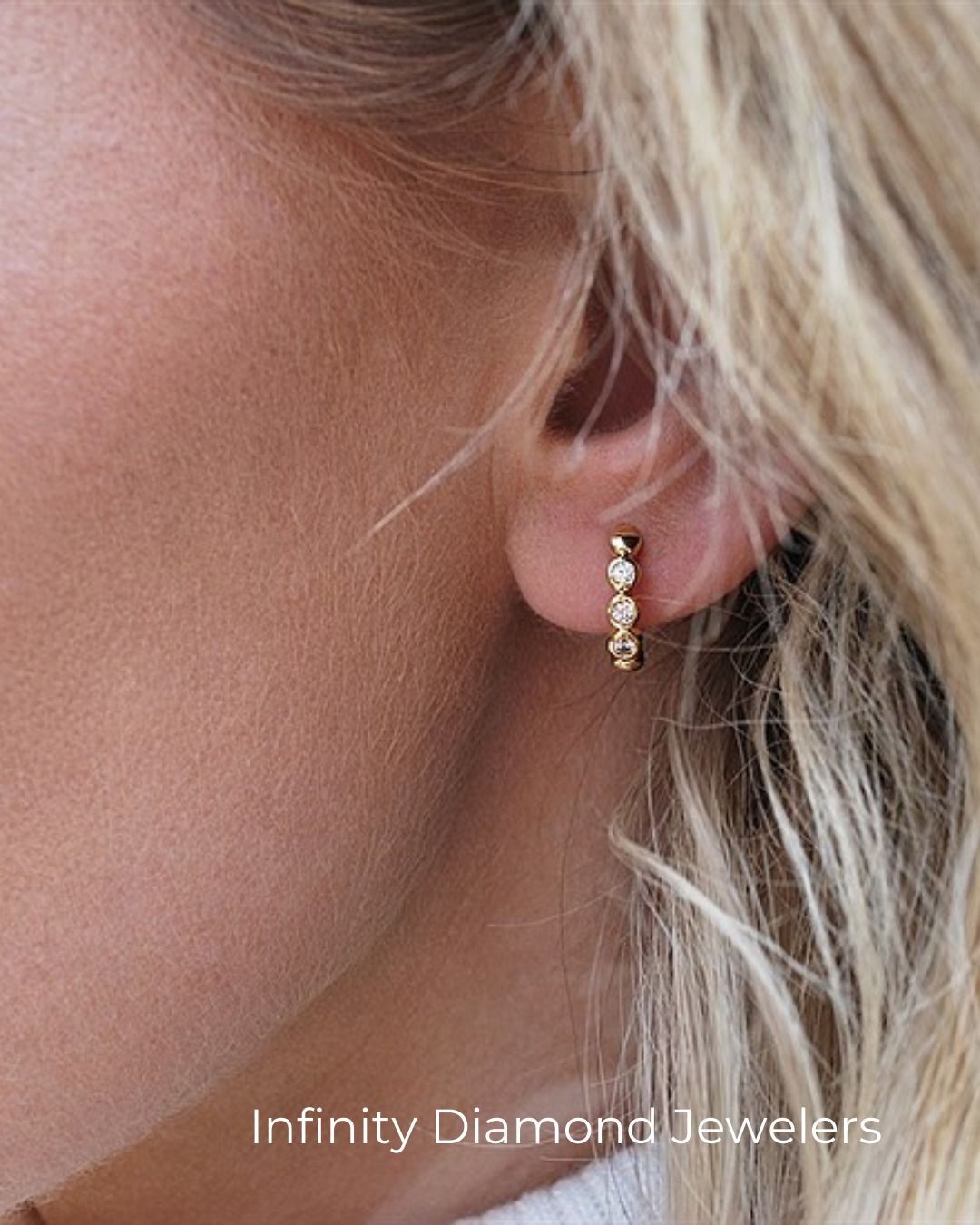 A woman's ear with a gold hoop earring adorned with small, clear gemstones.