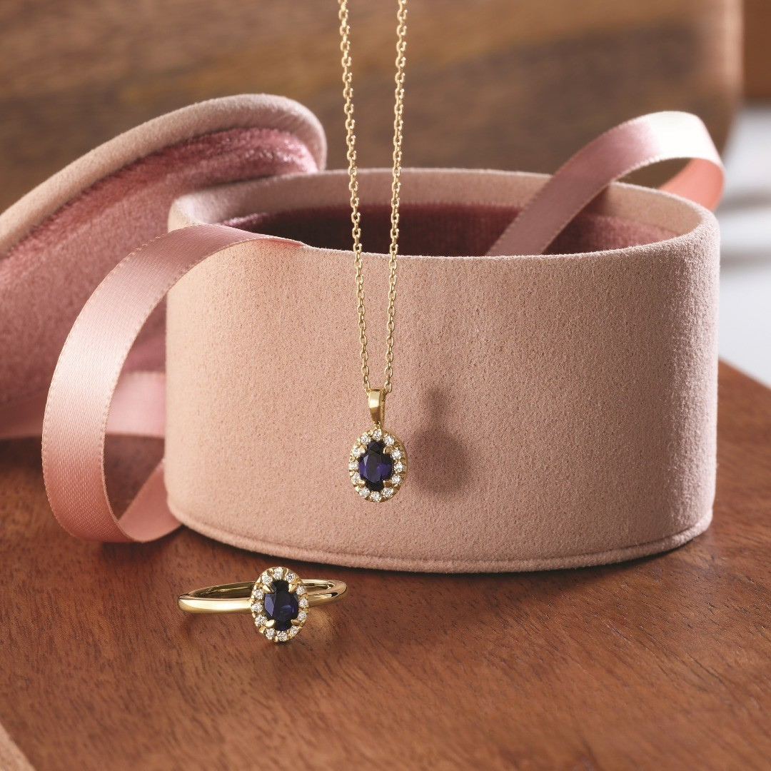 Gold jewelry set with sapphire and diamond halo; necklace in a velvet box, ring nearby.
