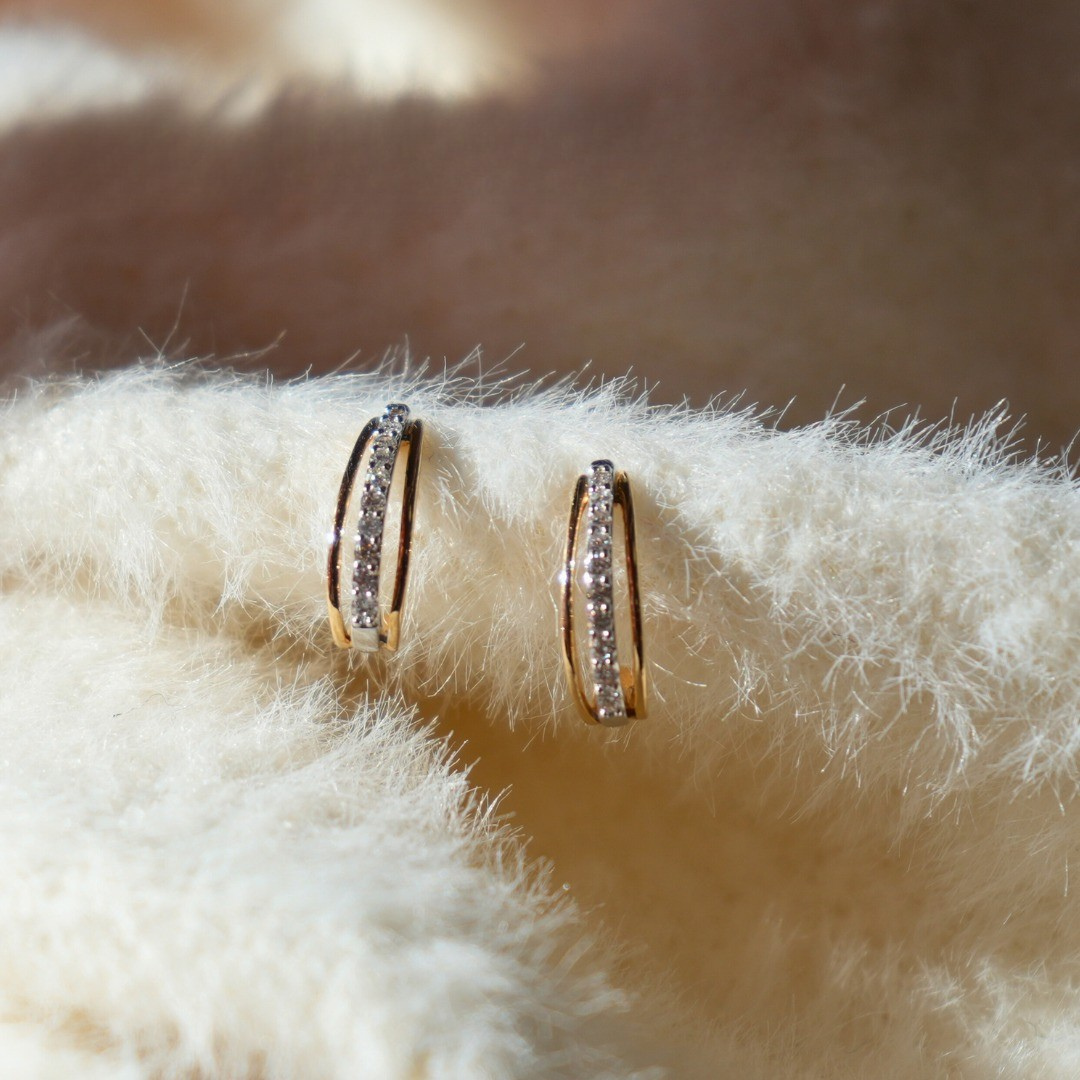 Gold hoop earrings with small crystals on fluffy white material.