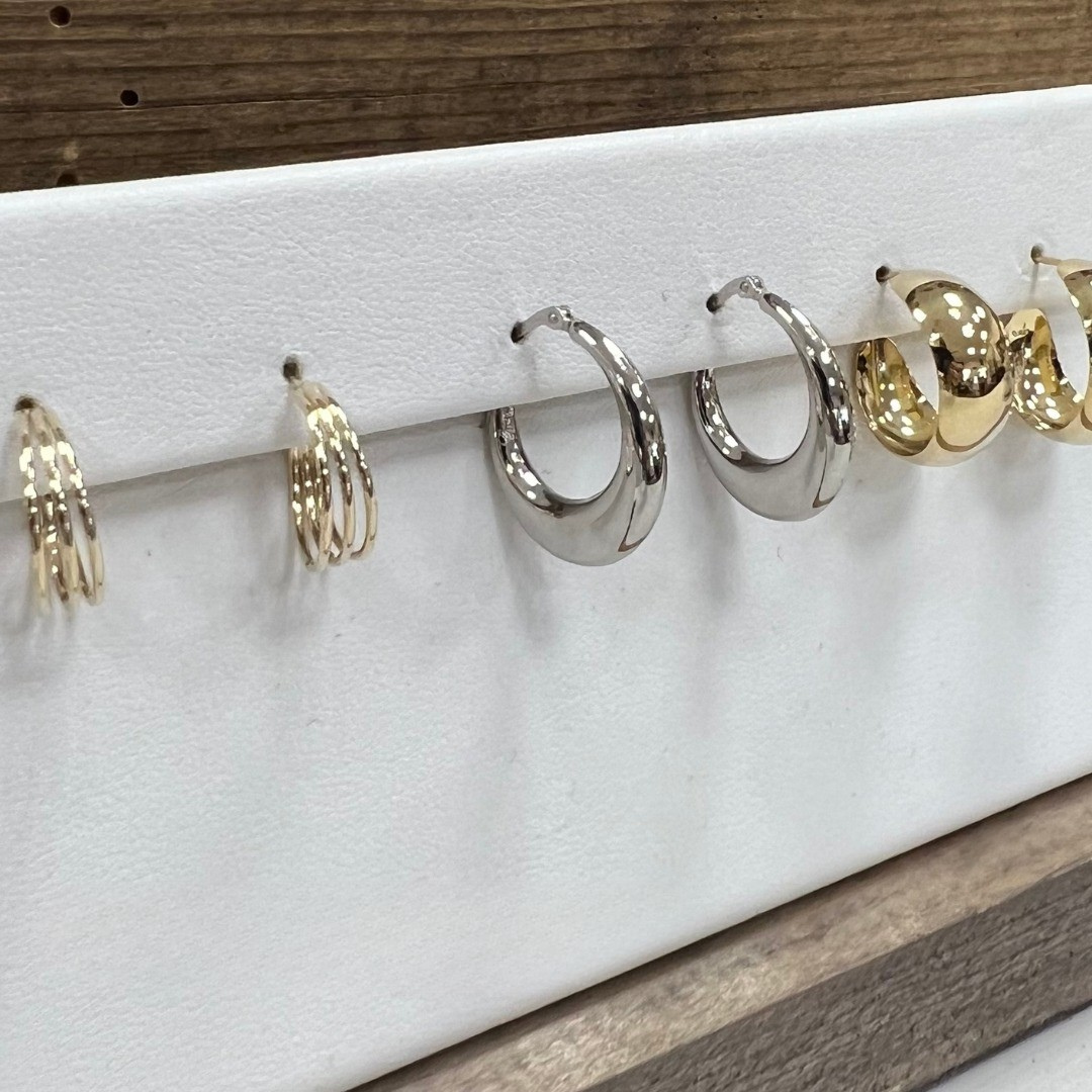 Earrings on display: gold and silver hoops, various sizes, arranged on white stand.