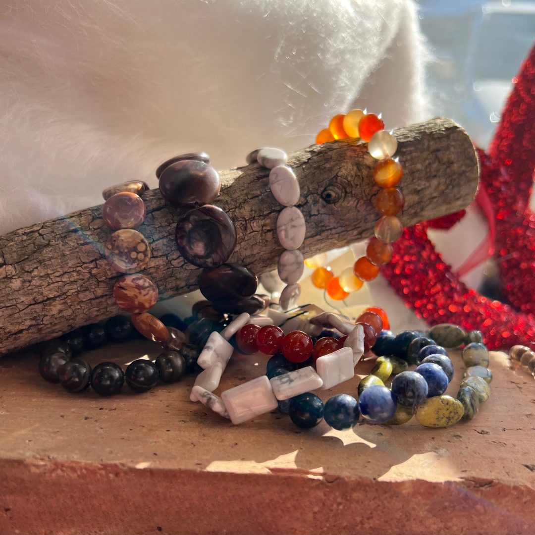 Colorful beaded bracelets displayed on a small log and terracotta surface.