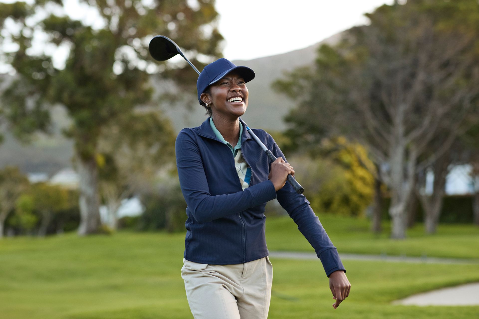Smiling Black woman in golf attire, holding a club, on a golf course. Smiling Black woman in golf attire, holding a club, on a golf course.
