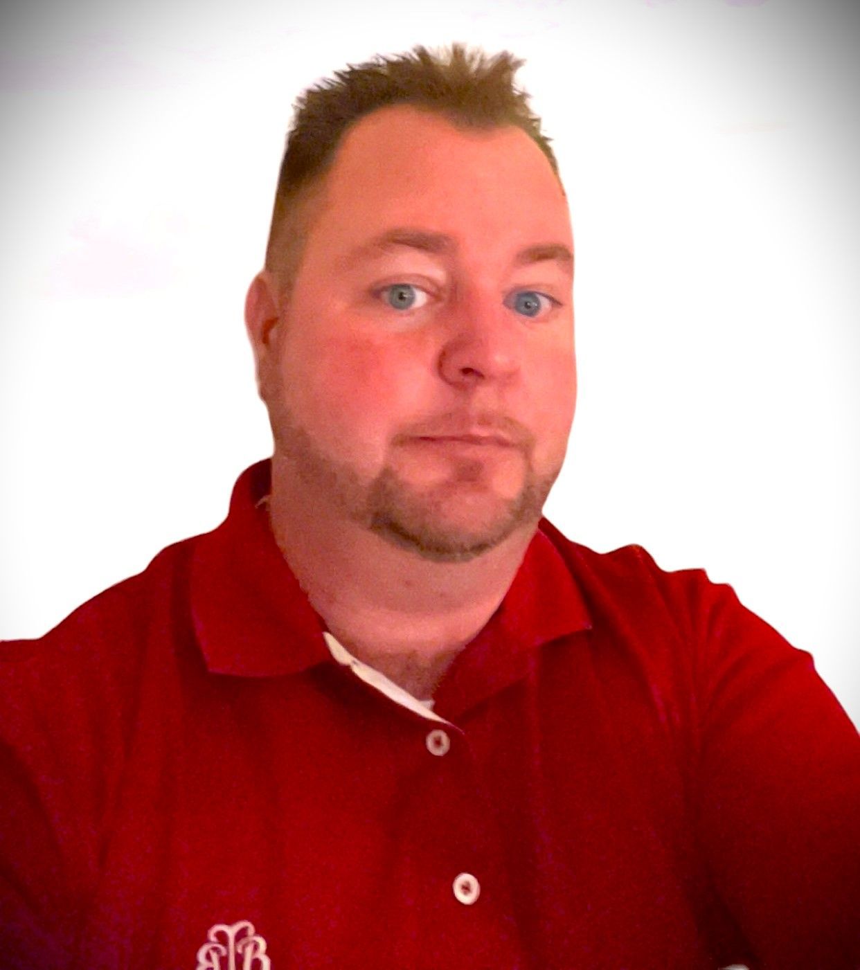 A man with a beard is wearing a red polo shirt