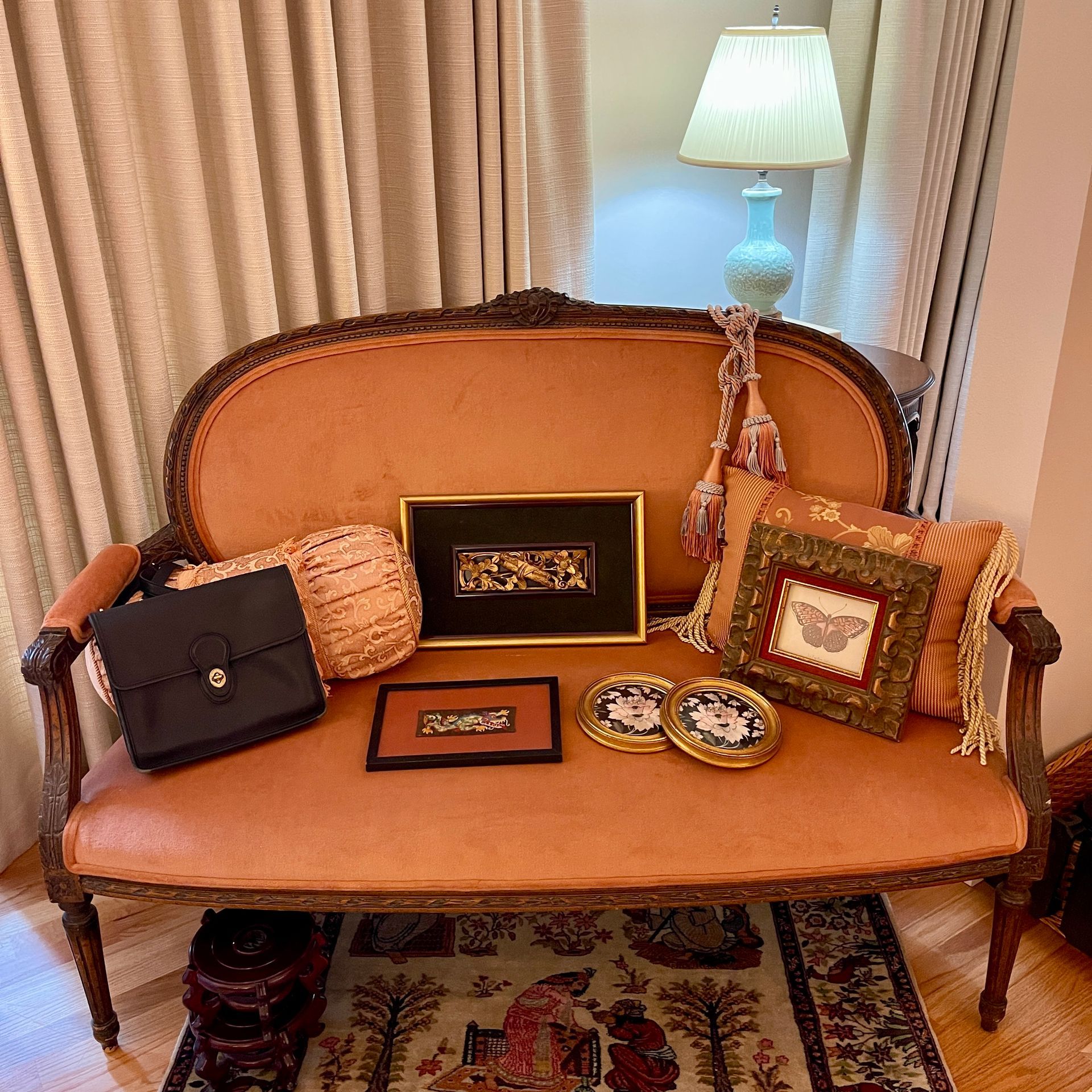 Ornate upholstered loveseat with decorative pillows and framed art; a lamp sits in the background.