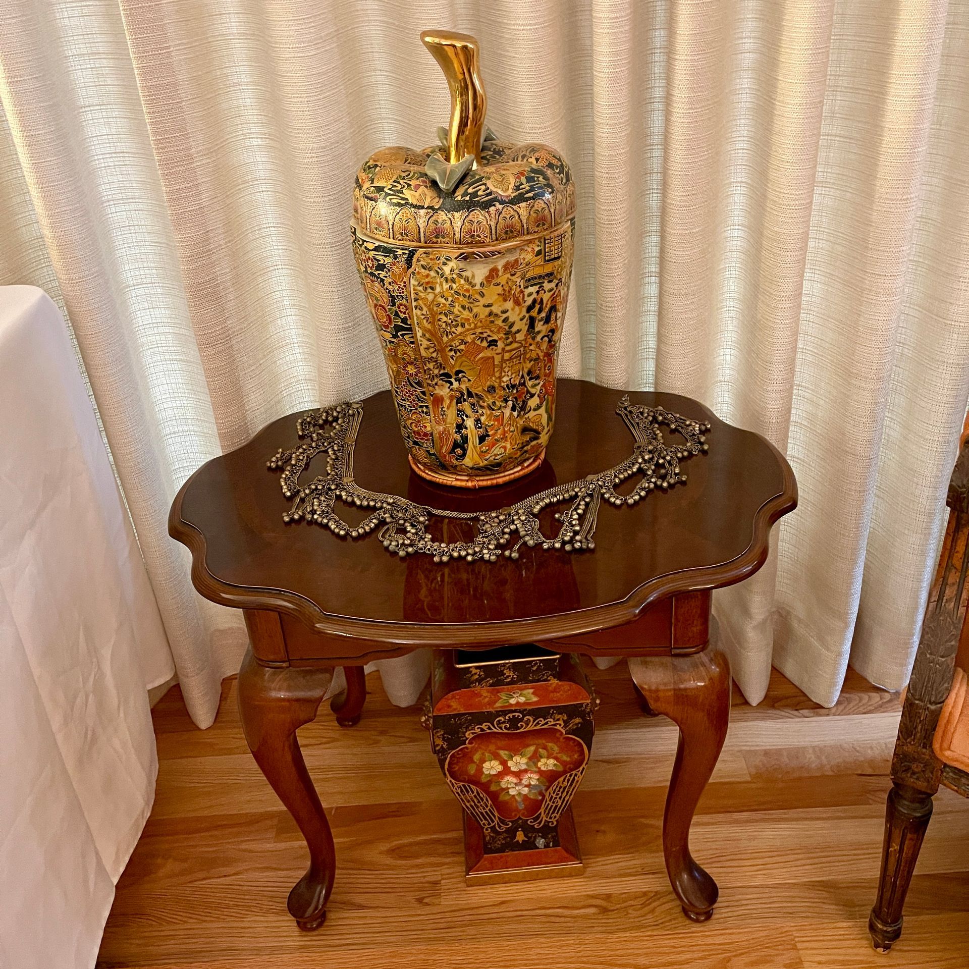 Ornate vase on a small wooden table with a decorative necklace; another vase beneath.