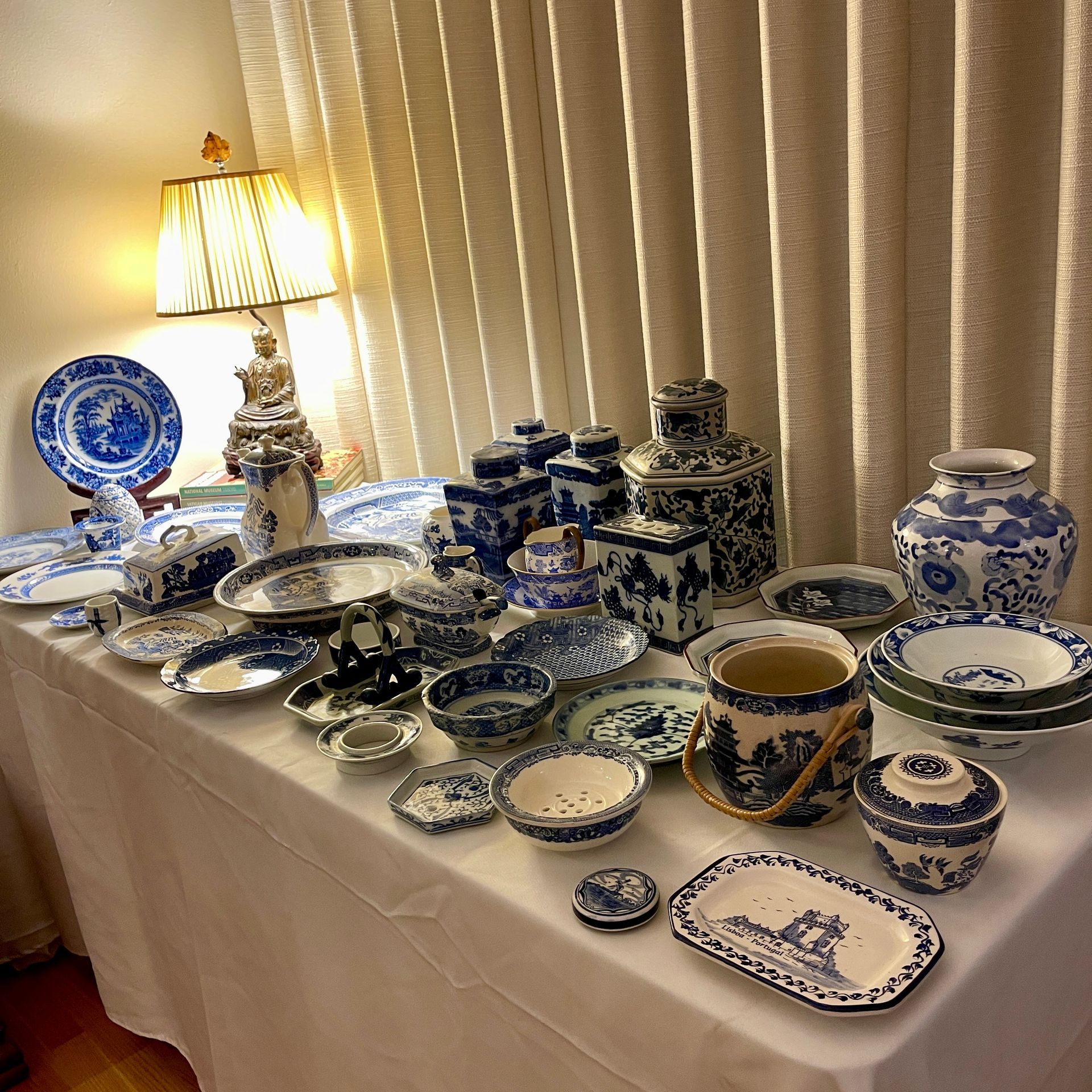 Table display of blue and white china pieces, lamp in the background.