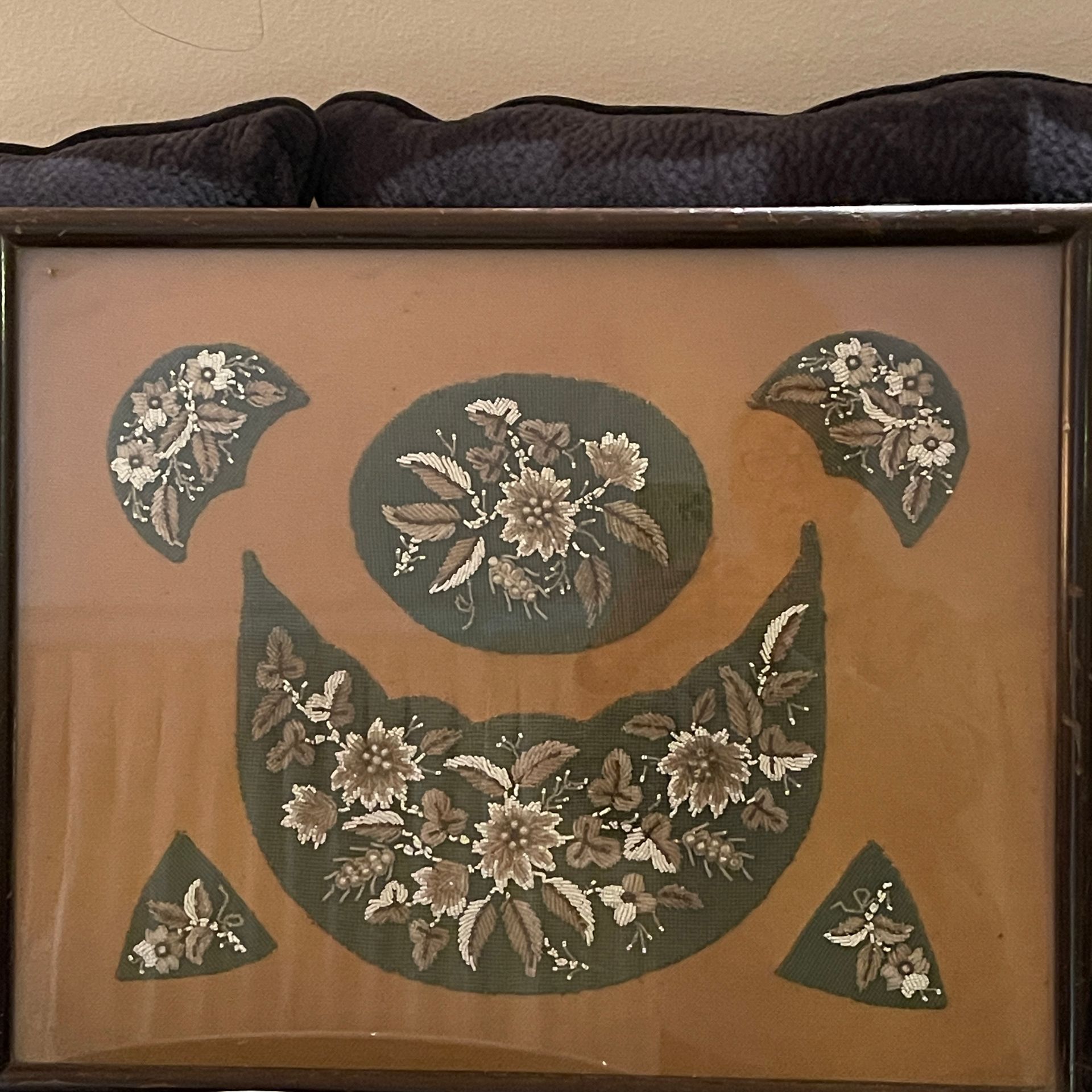 Framed textile art: green embroidered floral patterns on tan background.