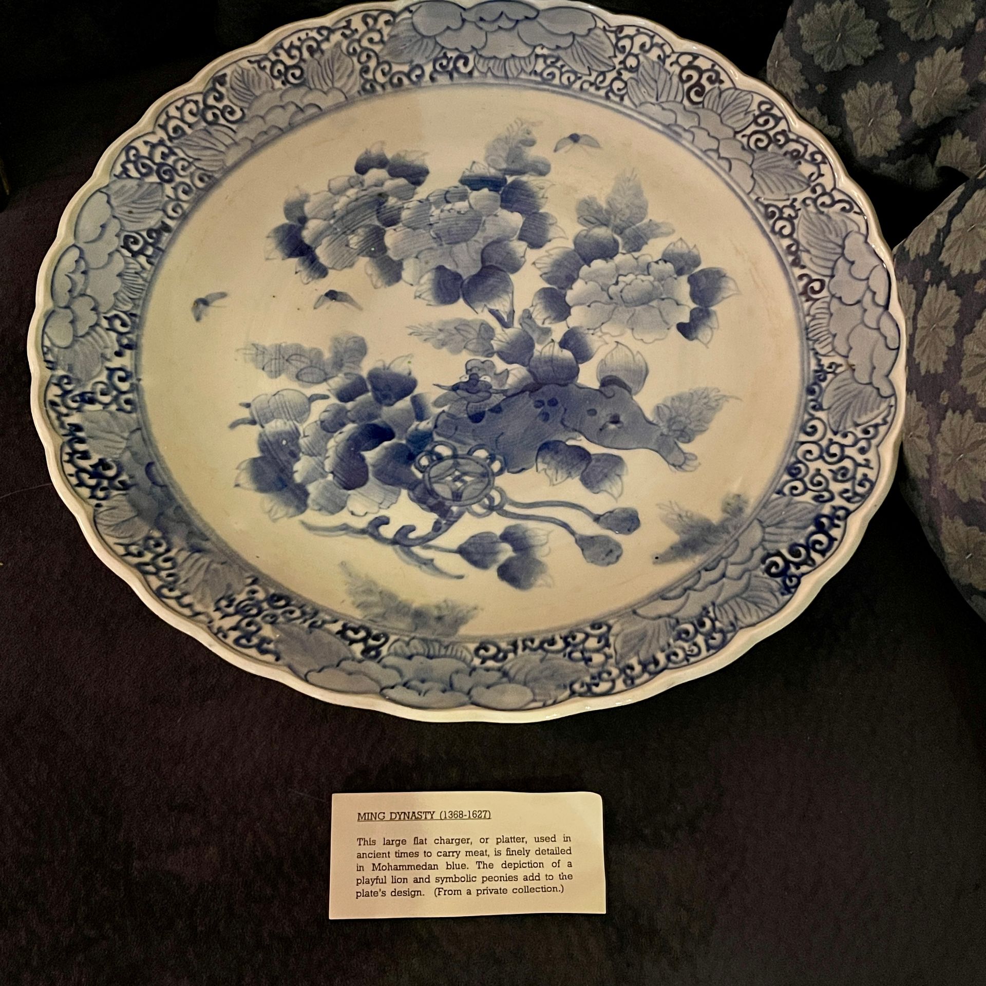 Blue and white porcelain plate with floral design and scalloped edge, displayed on a dark surface.