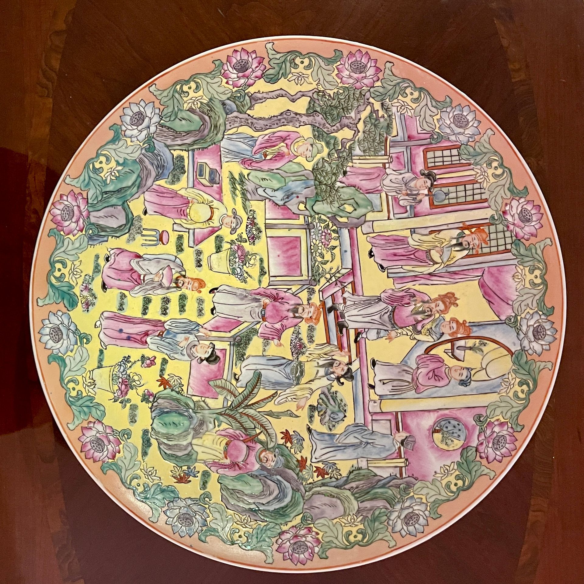 Decorative porcelain plate with a yellow central scene, pink buildings, and a floral border.