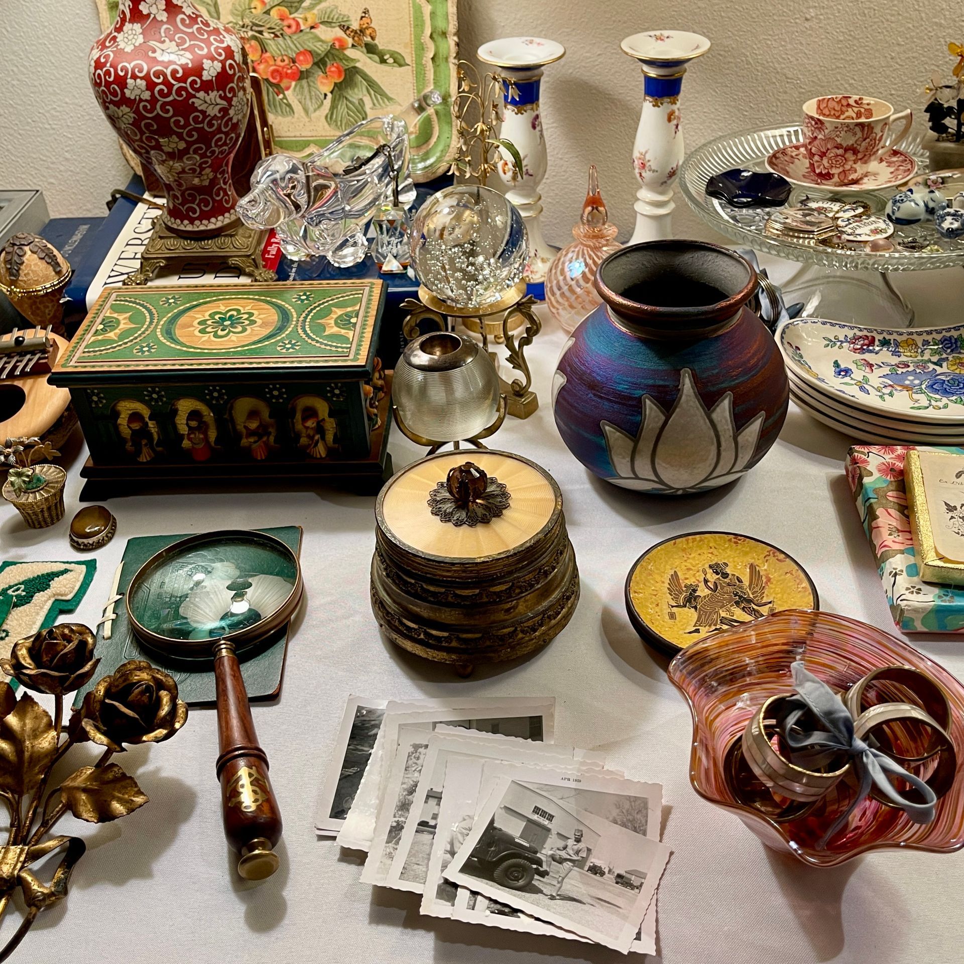 A table displaying numerous vintage items: vases, jewelry, photos, dishes, and decorative objects