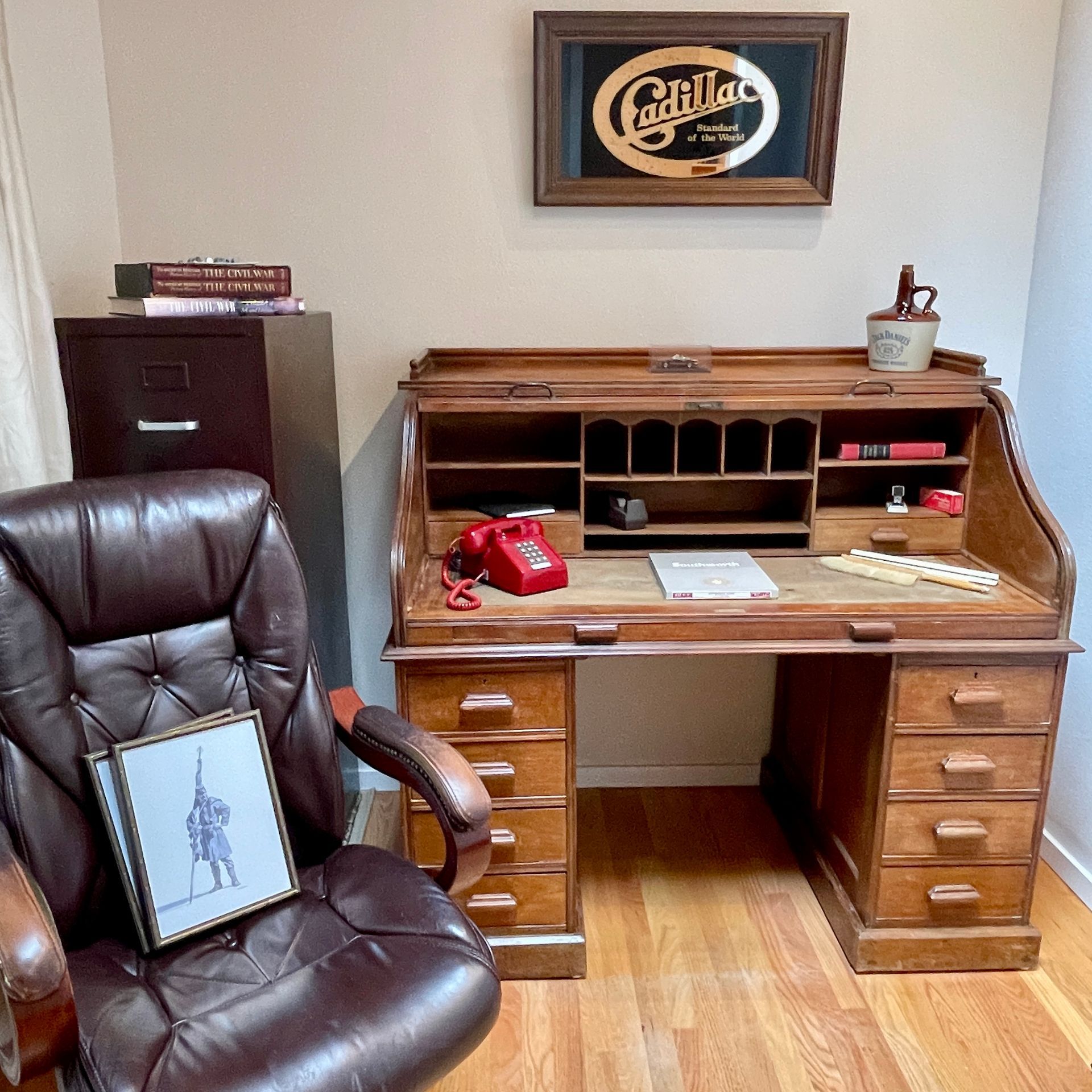 Vintage office: wooden desk with roll-top, leather chair, filing cabinet, Cadillac sign, phone.