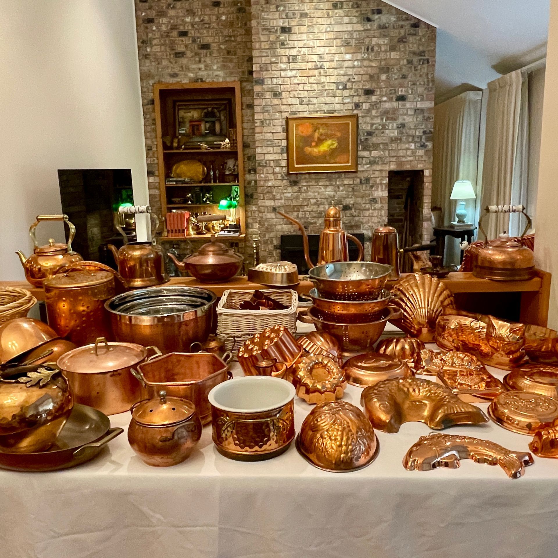 Copper cookware and molds displayed on a table in front of a brick fireplace.