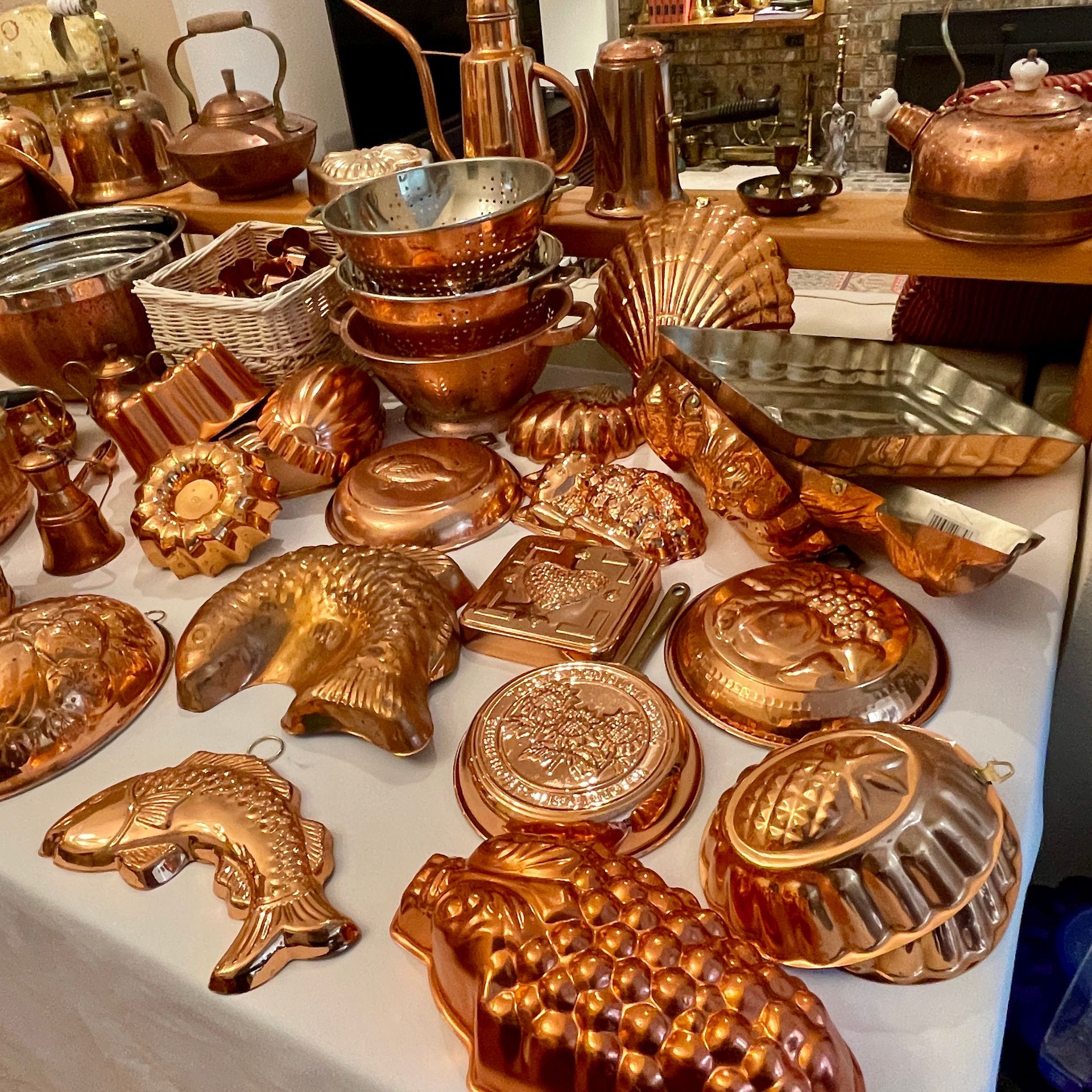 Collection of copper kitchenware, including molds, pots, and kettles, displayed on a table.