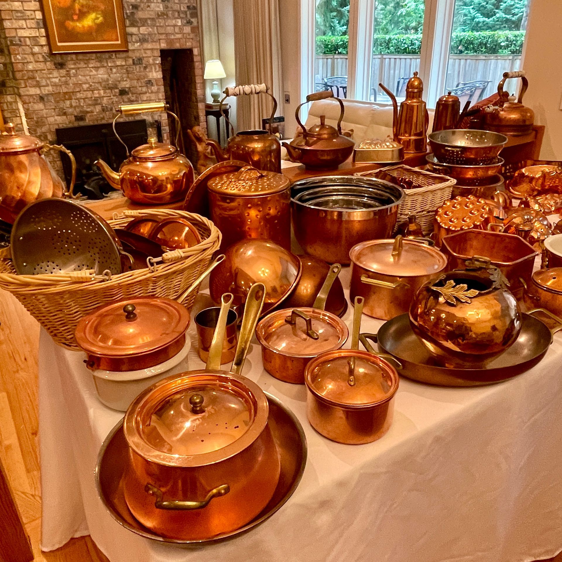 A table overflowing with various copper cookware items in a sunlit room.