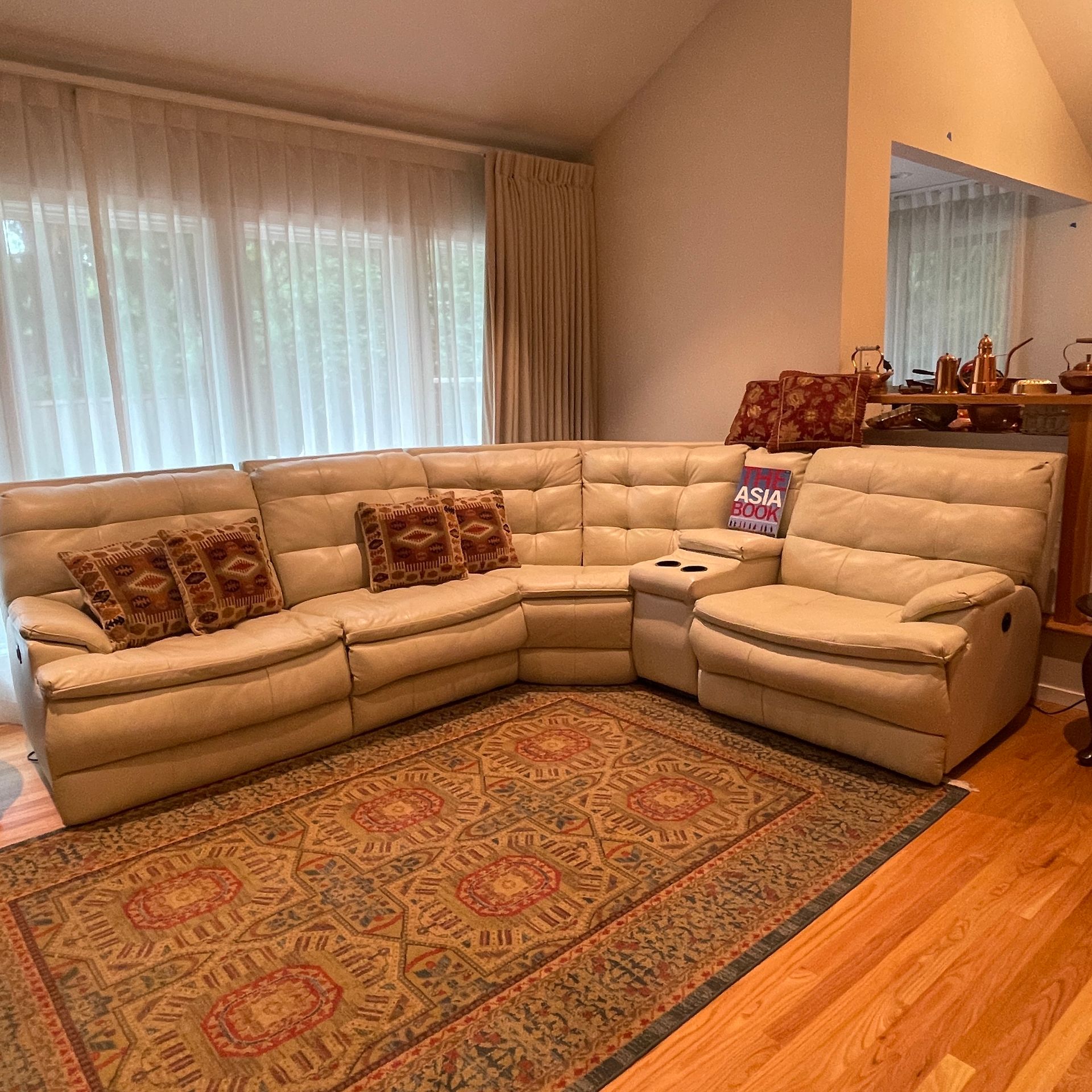 Beige sectional sofa and recliner, rug, pillows, window with curtains, wood floor, and side table.