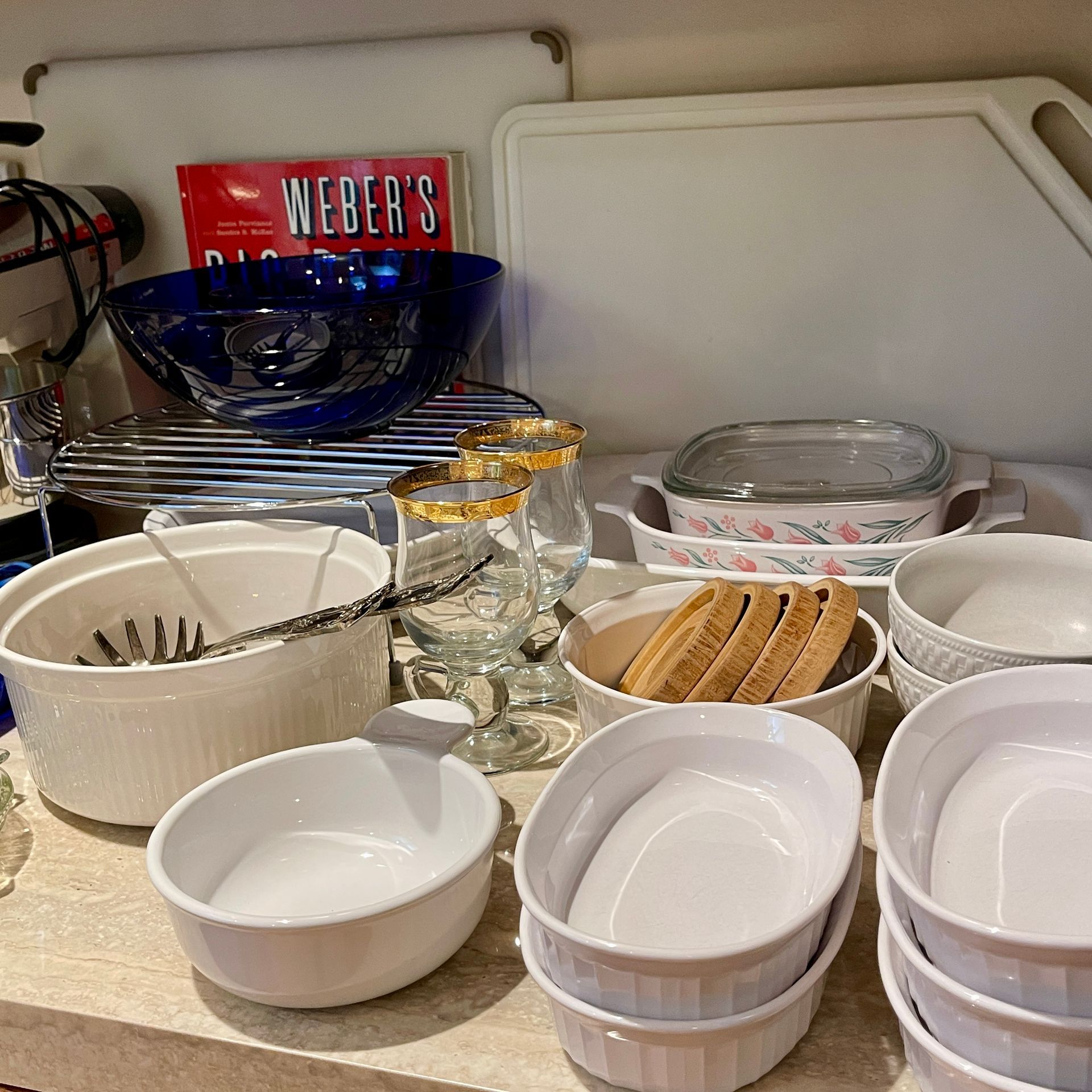 Kitchen counter with various white and blue serving dishes, cutting boards, cookbooks, and glassware.